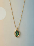 Gold necklace with a green pendant on a light background