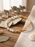 Pearl and gold bracelet on a wooden surface with leaves and shells