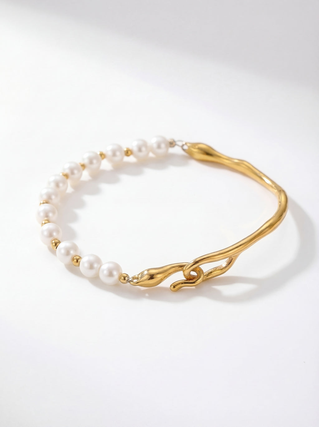 Gold bracelet with white pearls on a light gray background