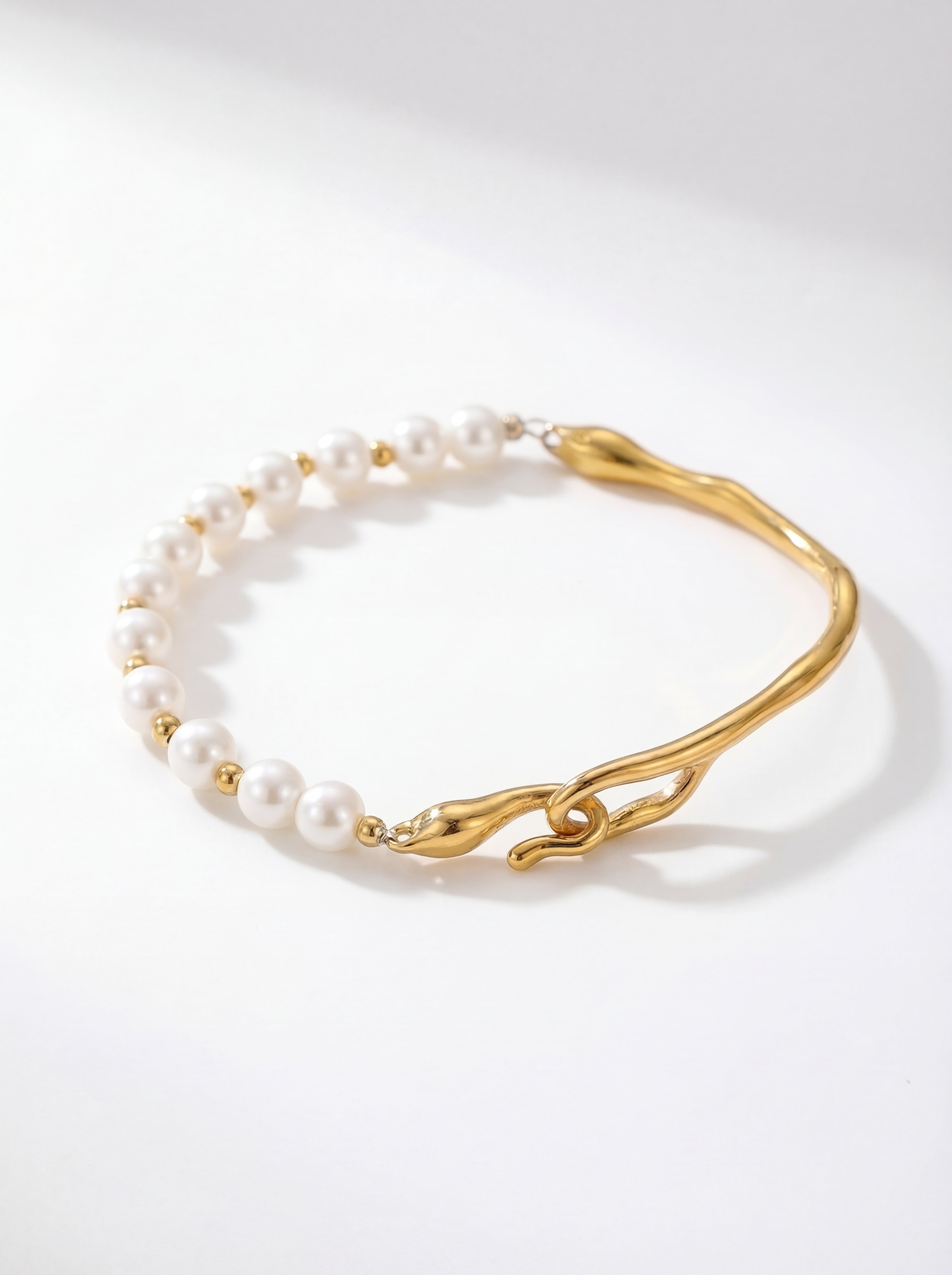 Gold bracelet with white pearls on a light gray background