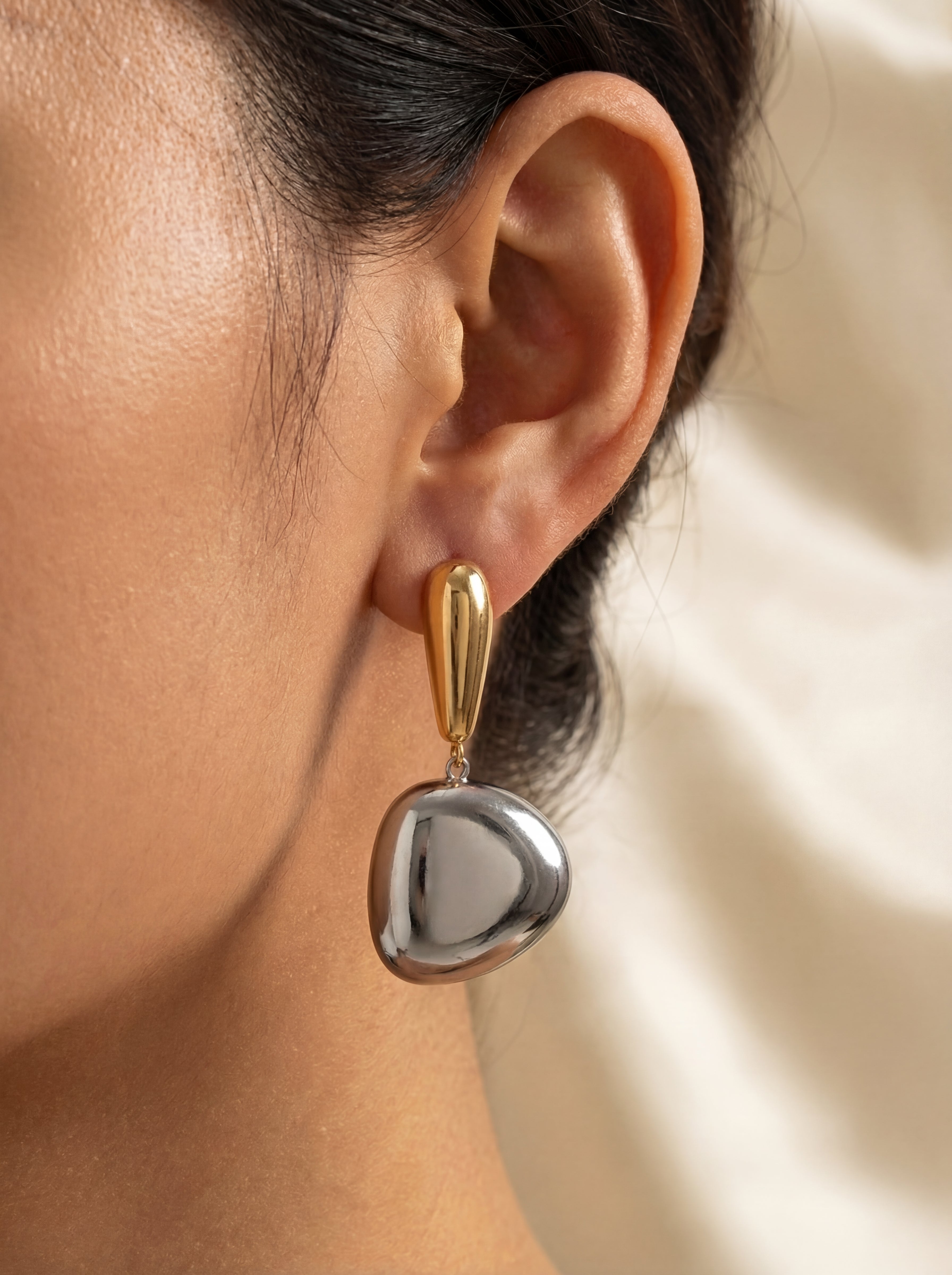 Close-up of an ear wearing a silver heart-shaped earring with gold accents.