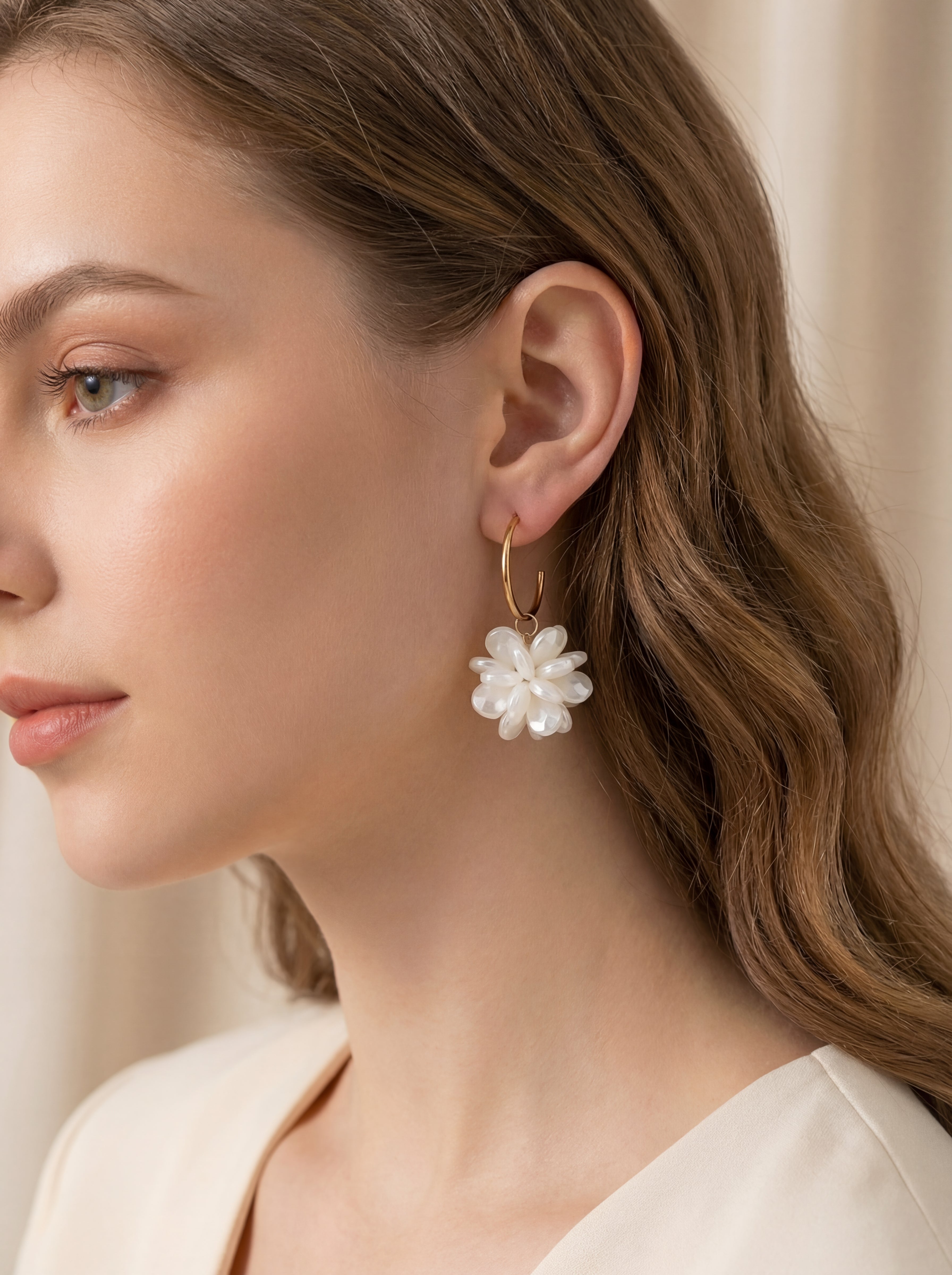 Woman wearing a floral earring with pearls against a neutral background