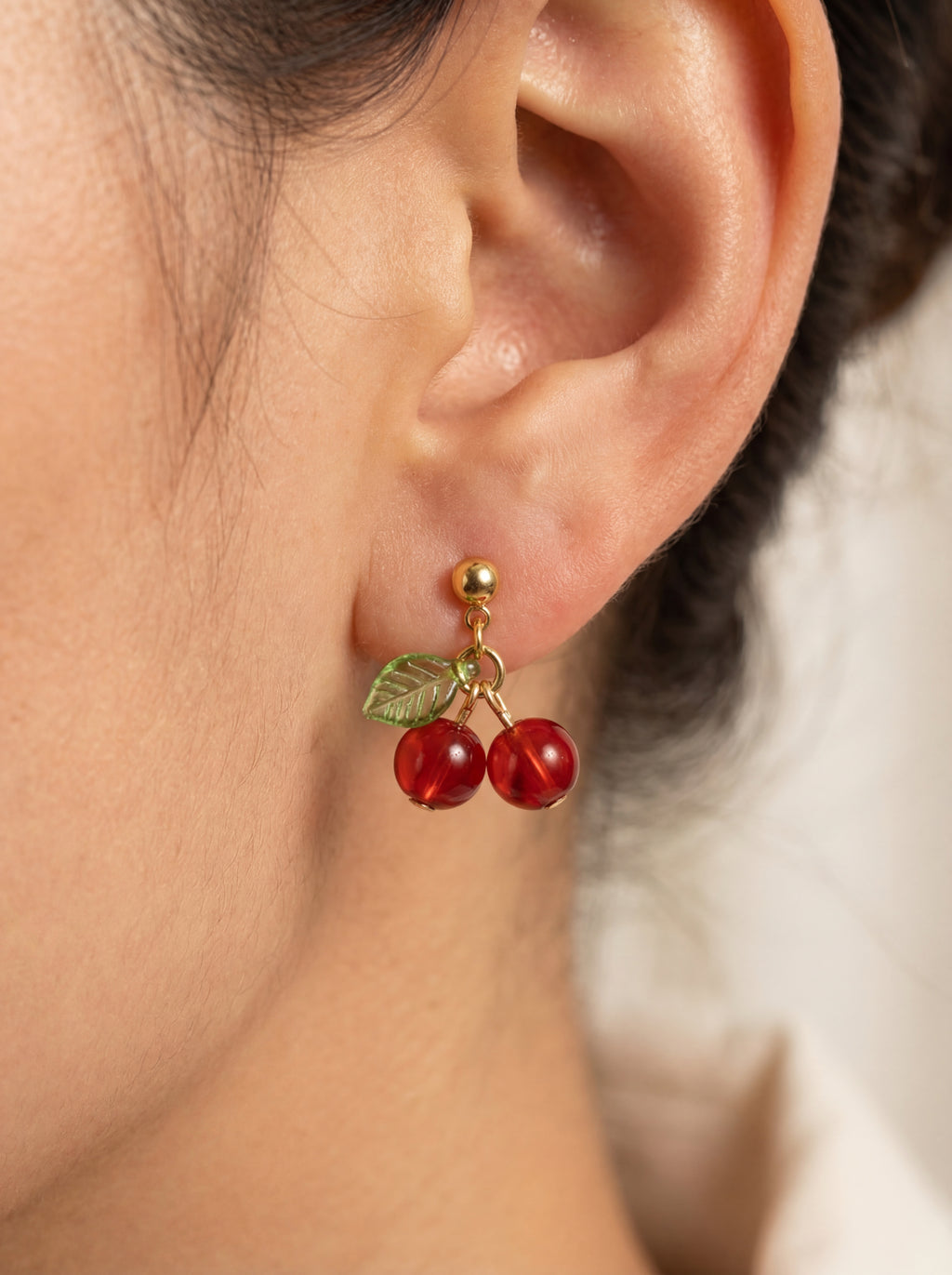 Close-up of an ear wearing a cherry-themed earring with a blurred background