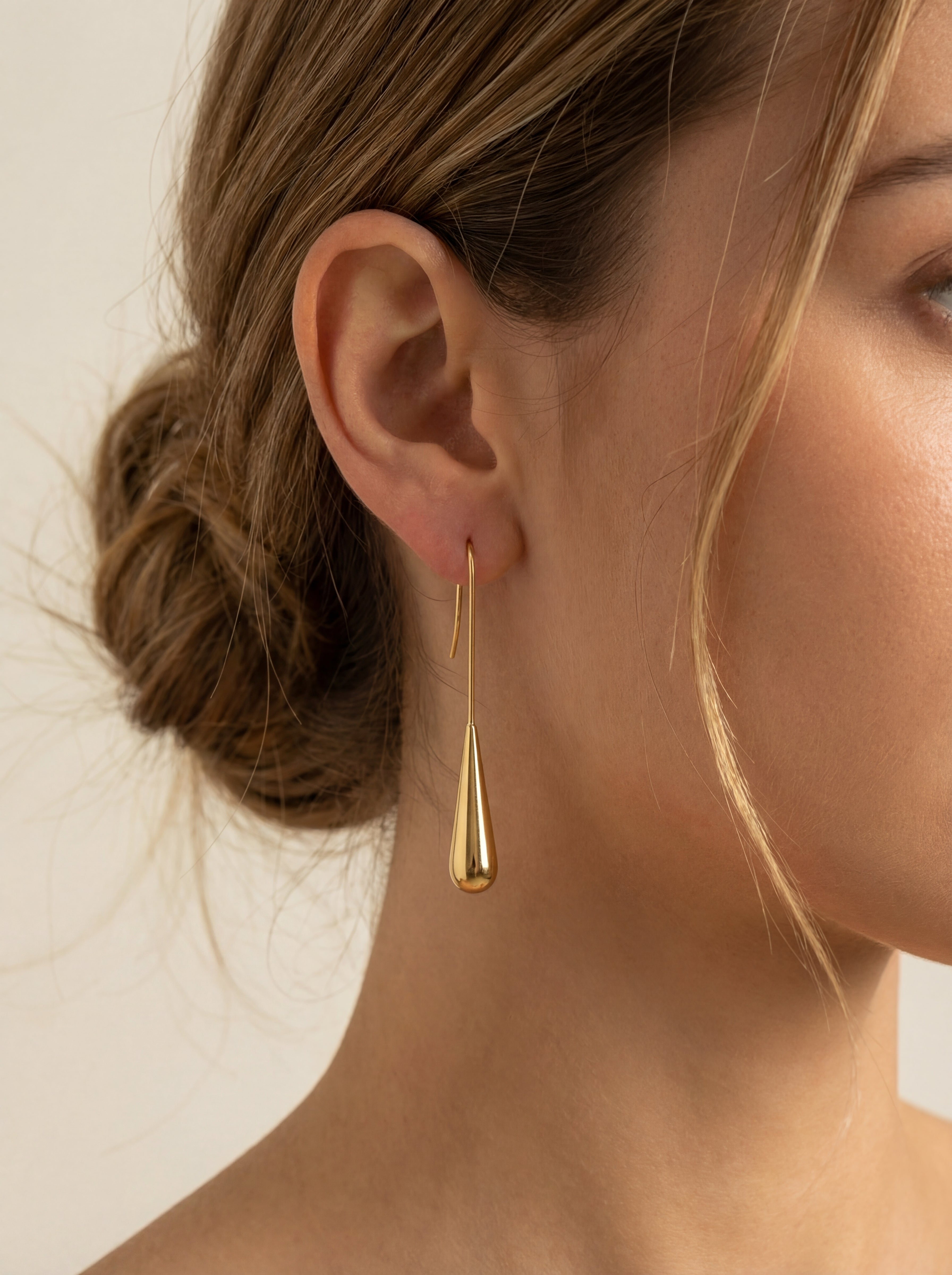 Gold teardrop earring worn by a person with a neutral background