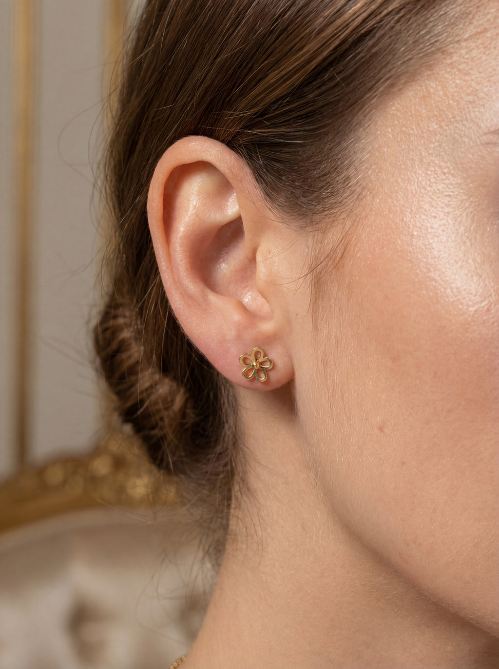 Close-up of an ear wearing a gold flower earring with a blurred background