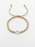 Gold beaded bracelet with a daisy charm on a white background