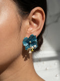 Close-up of an ear wearing a blue floral earring with a bee and pearl detail.