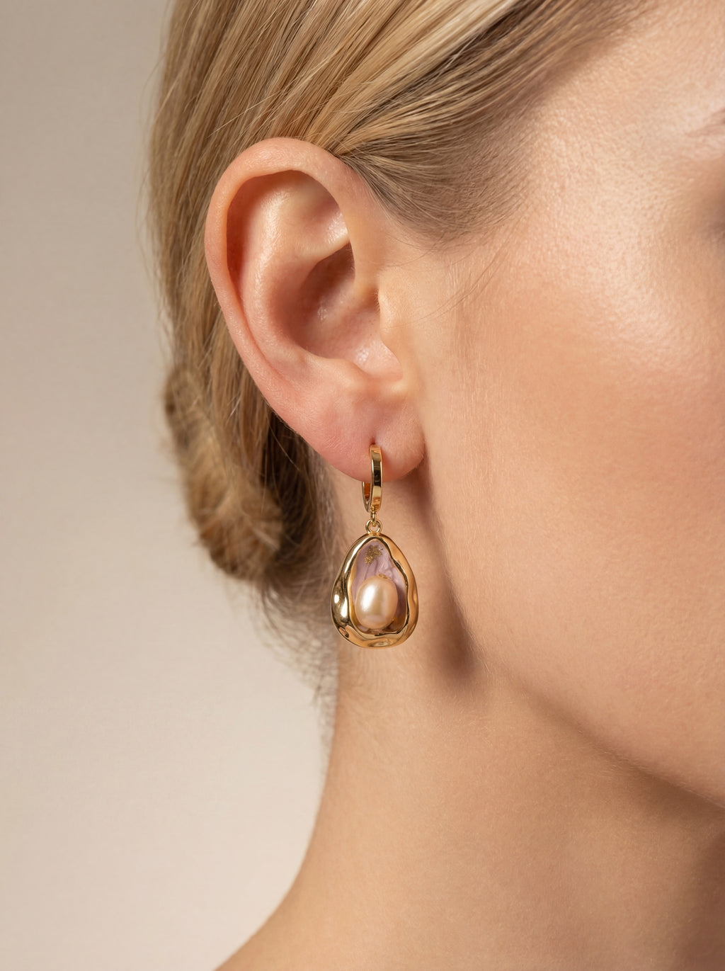 Gold teardrop earring worn by a model on a neutral background