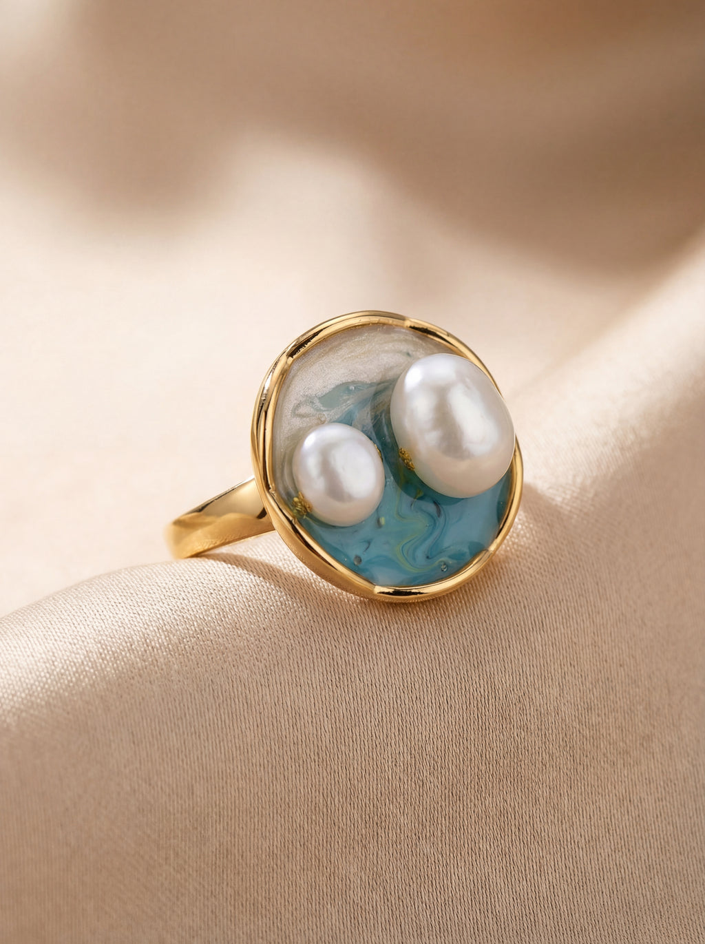 Gold ring with pearls and blue accents on a beige fabric background
