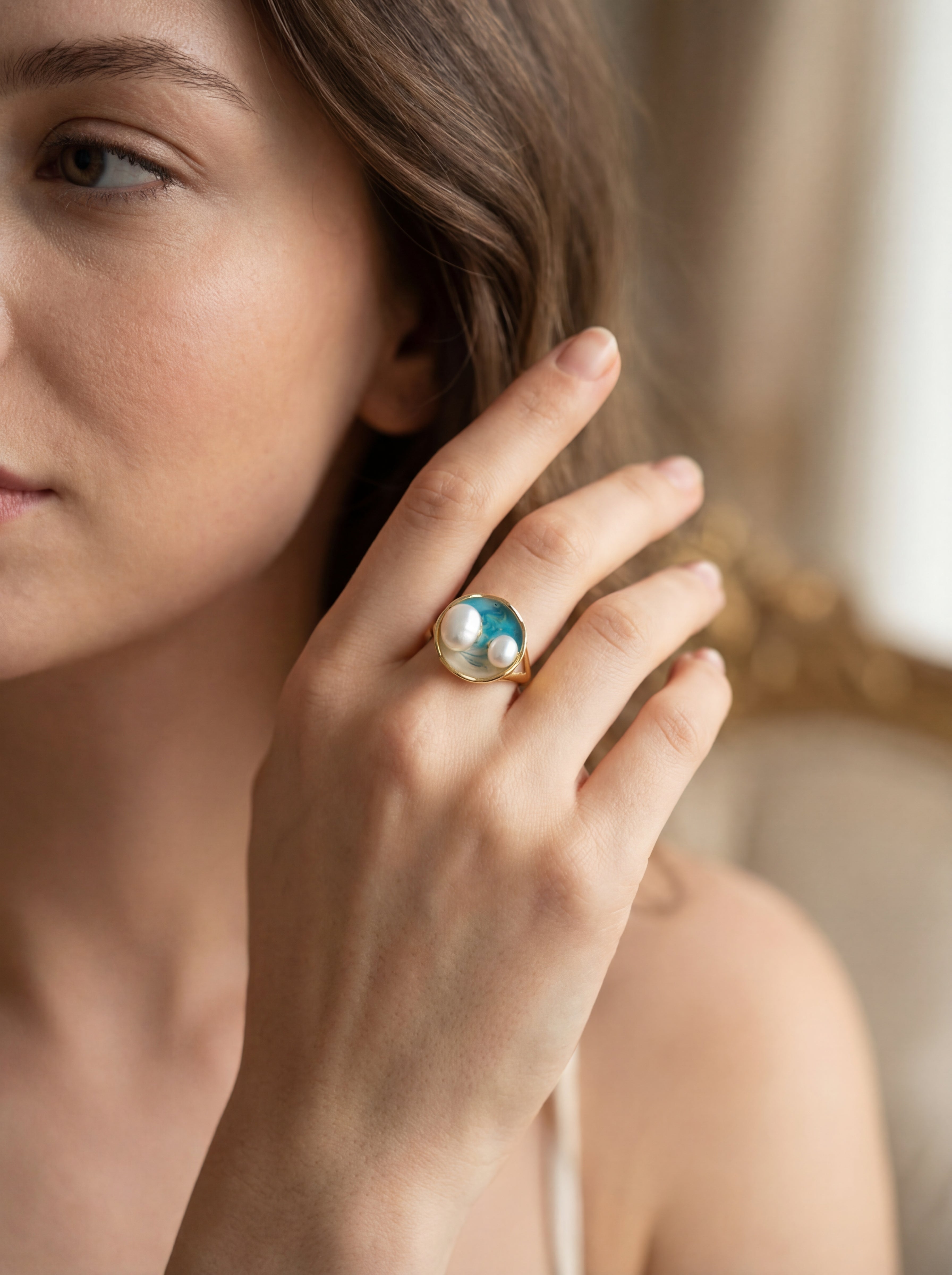 Close-up of a woman wearing a ring with a pearl and gemstone on a blurred background