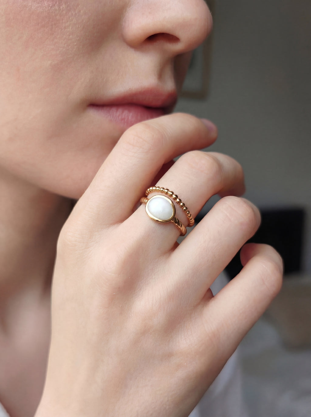 Close-up of a hand wearing a gold ring with a white stone, blurred background