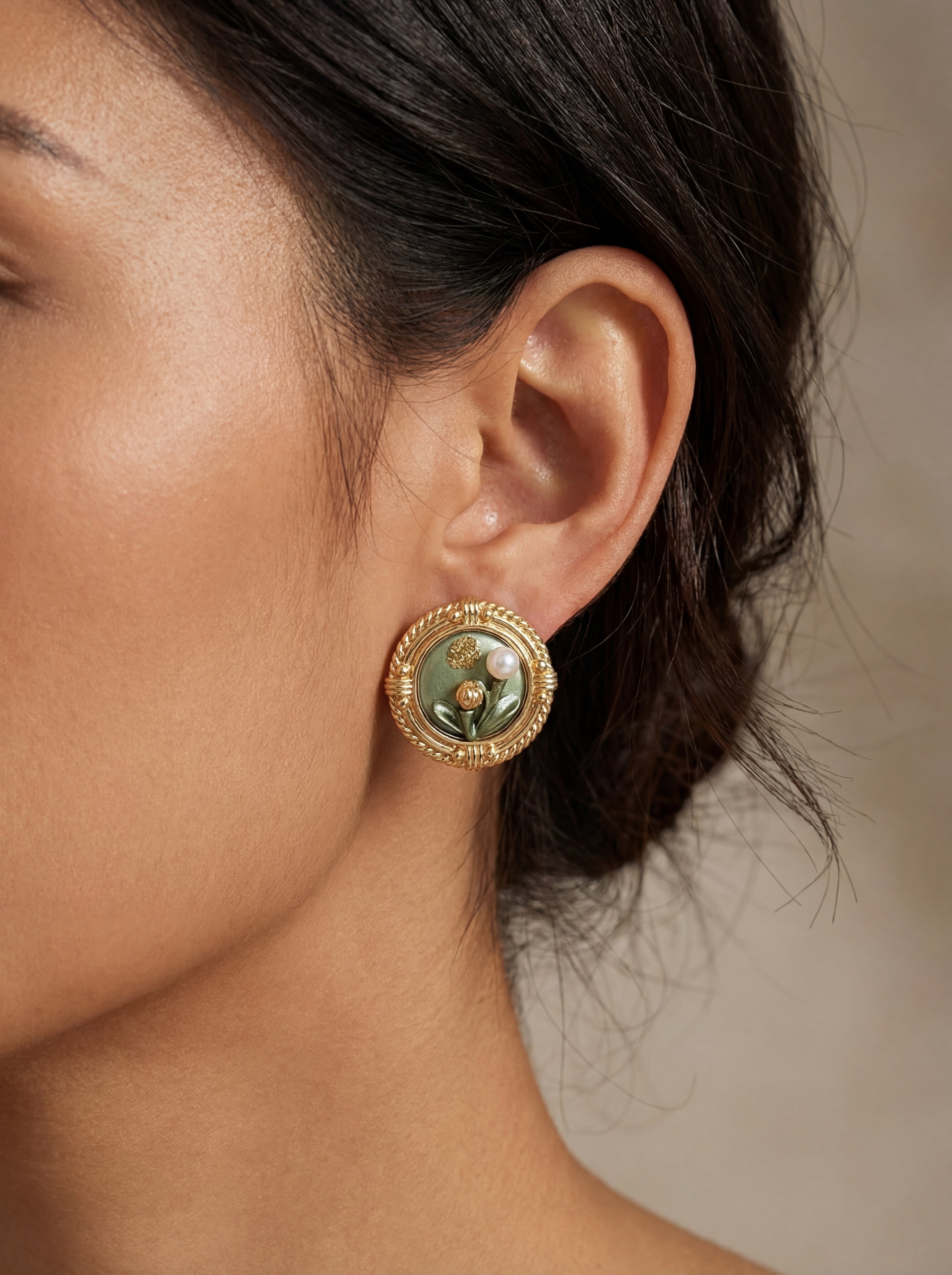 Close-up of a person wearing a gold earring with a green gemstone on a neutral background