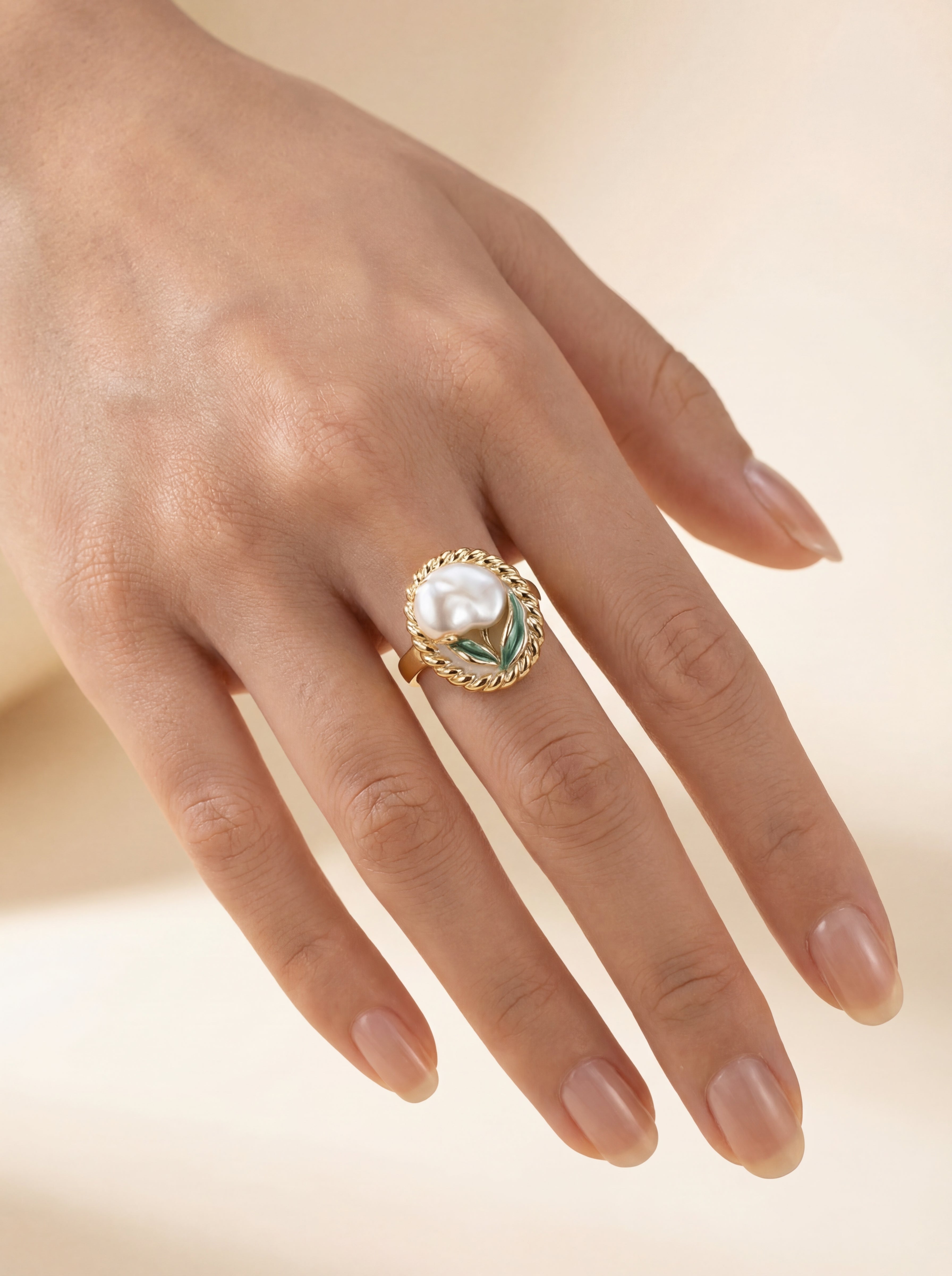 Gold ring with a pearl on a hand against a beige background