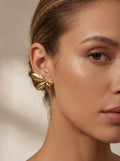 Close-up of a woman wearing gold leaf earrings with a neutral background