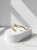 Gold bracelet on a white pedestal with a minimal background