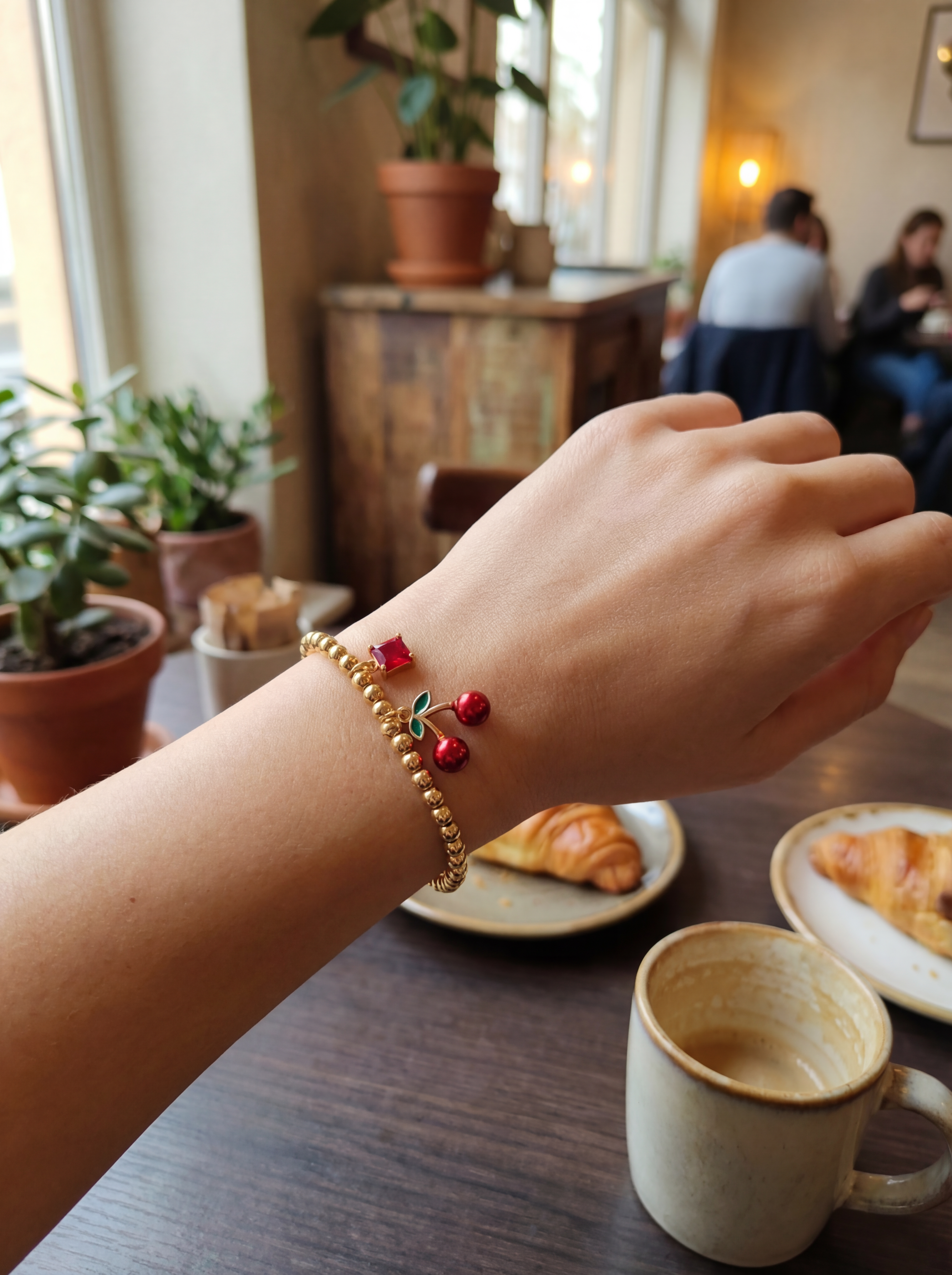 Hand wearing a gold bracelet with red beads in a cafe setting