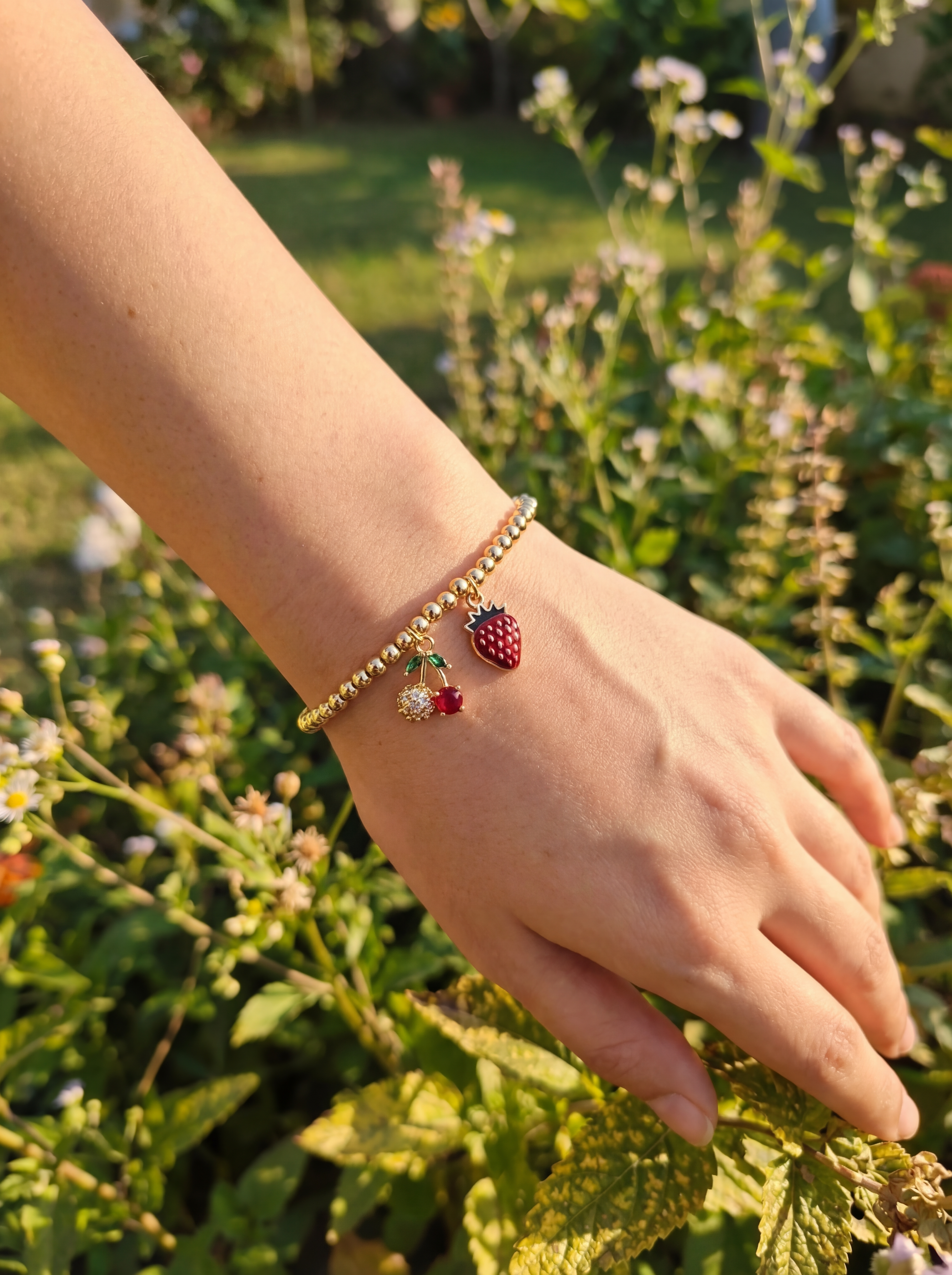 Hand wearing a bracelet with strawberry charm in a garden setting