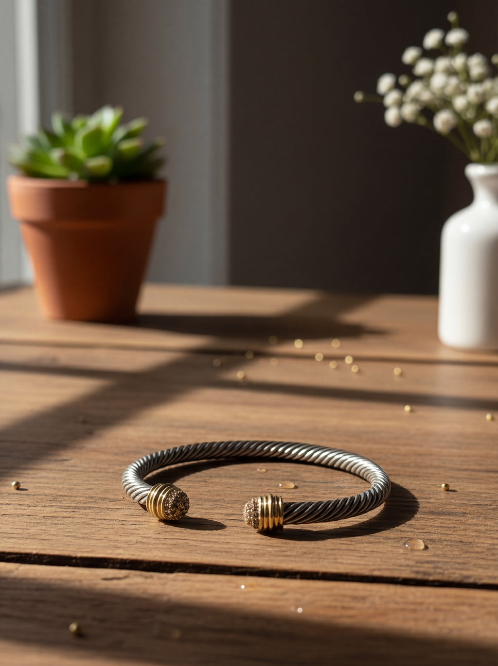 Silver and gold bracelet on a wooden surface with plants in the background