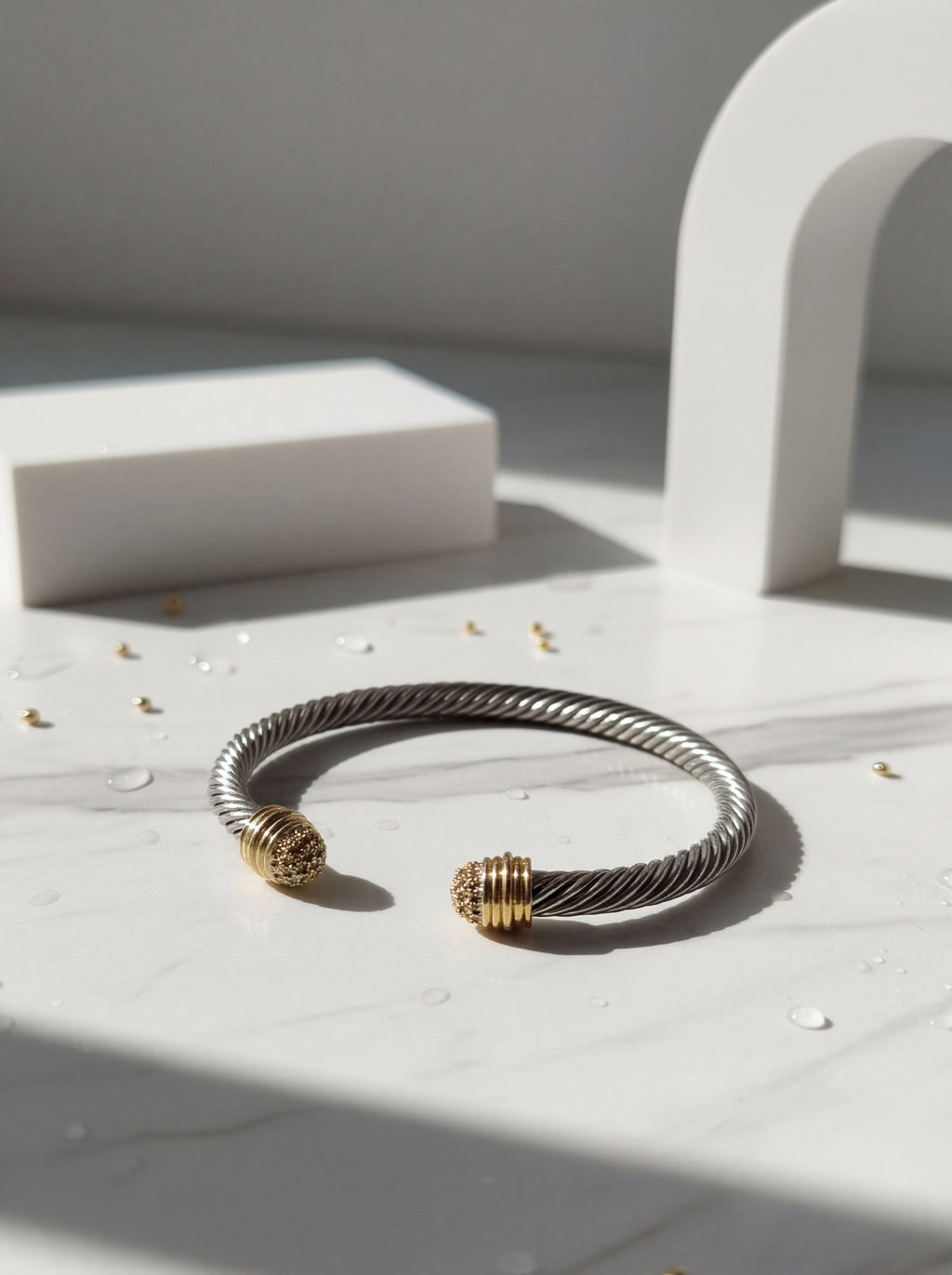 Silver and gold bracelet on a light surface with architectural elements in the background