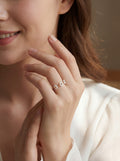 Close-up of a woman's hand wearing a delicate ring with small stones, against a neutral background.