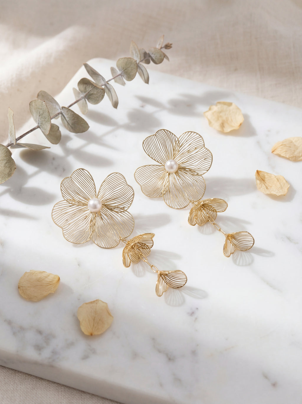 Gold floral earrings with pearls on a marble surface