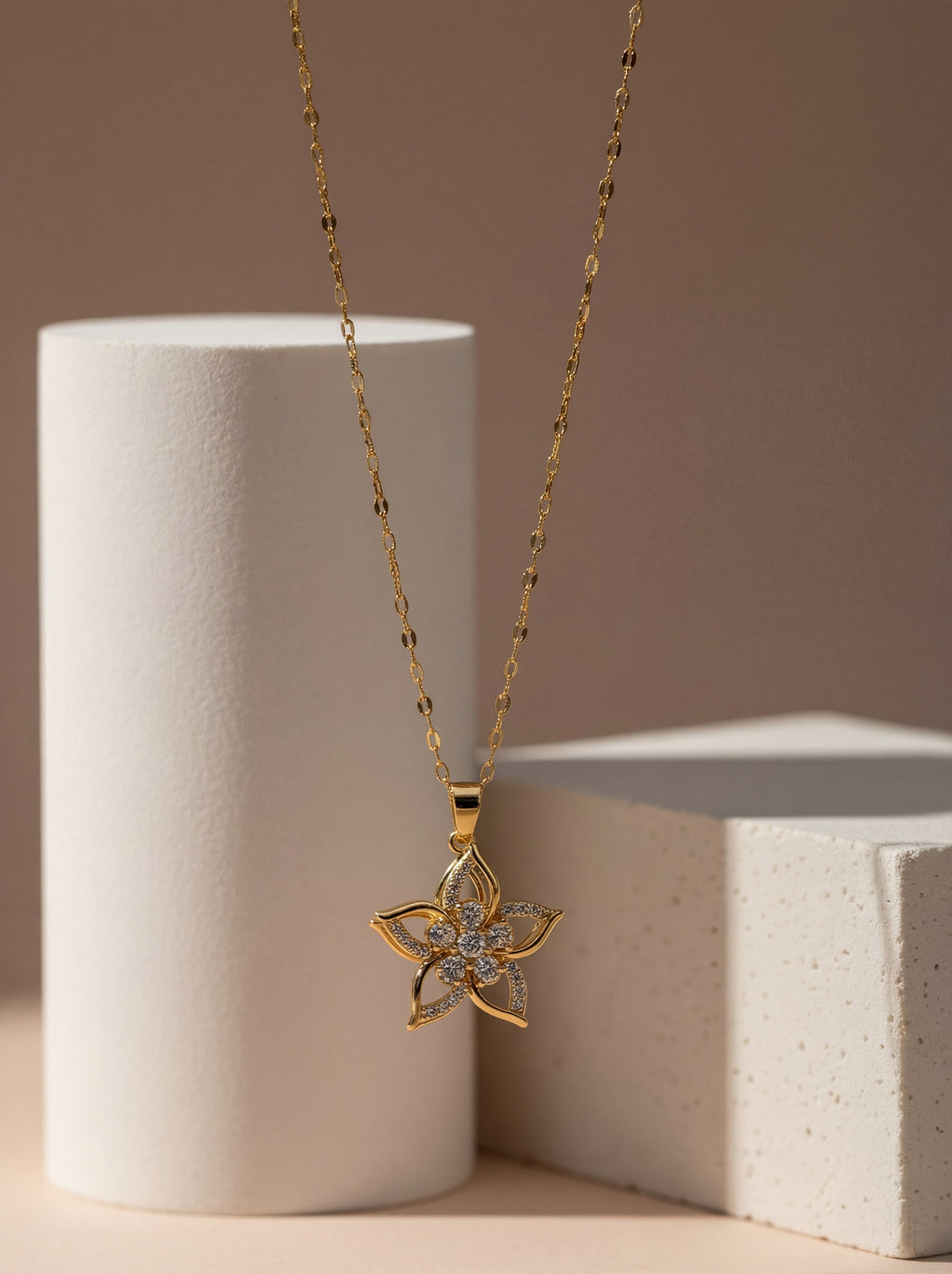 Gold necklace with a floral pendant on a neutral background
