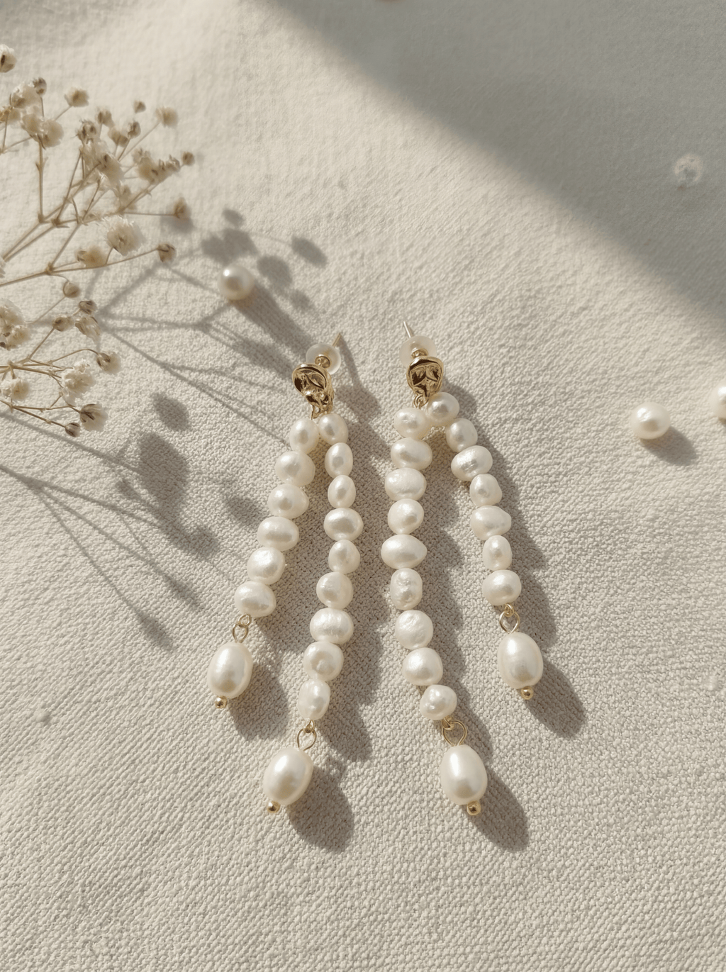 Pearl earrings on a light surface with dried flowers