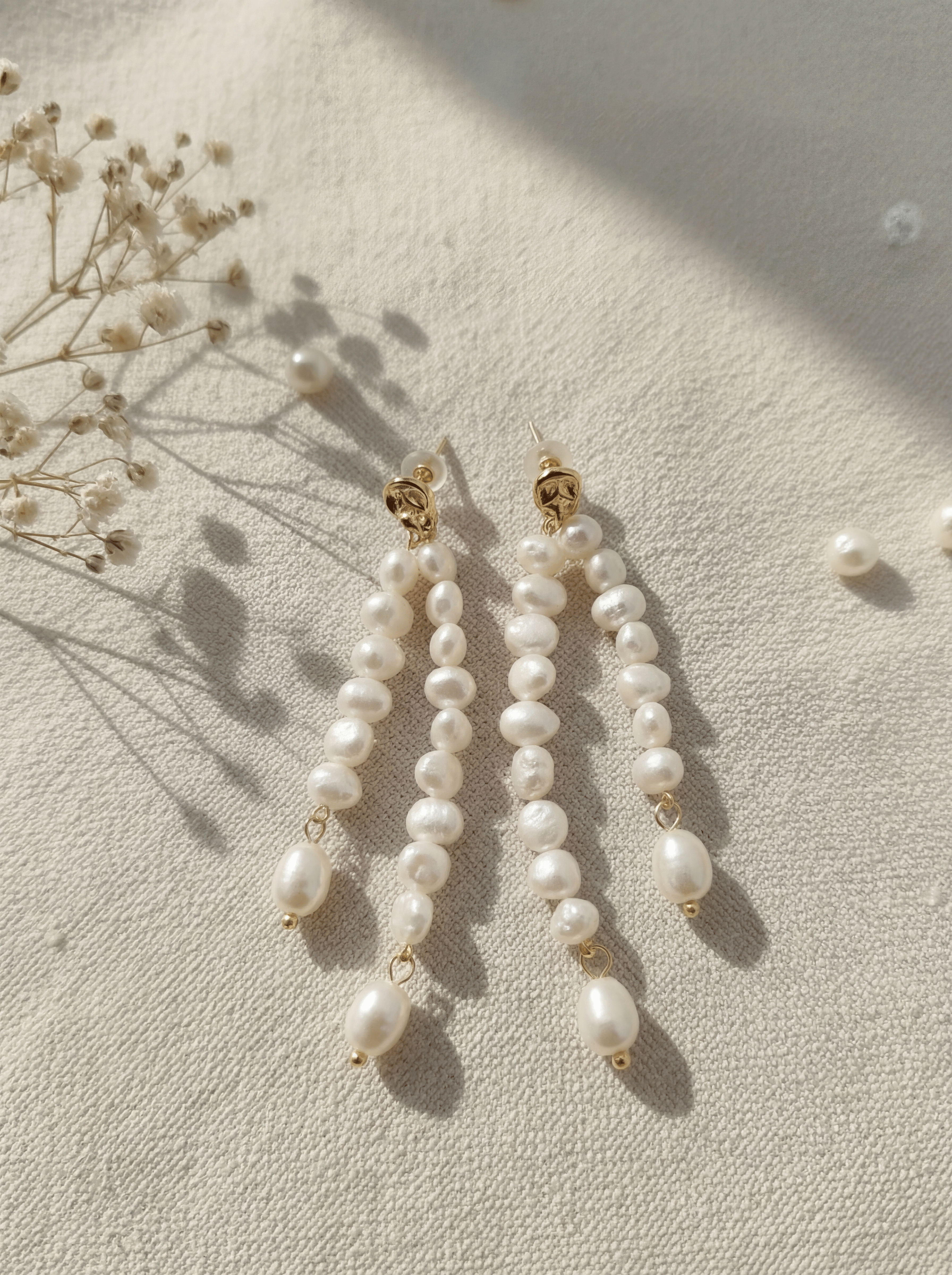 Pearl earrings on a light surface with dried flowers