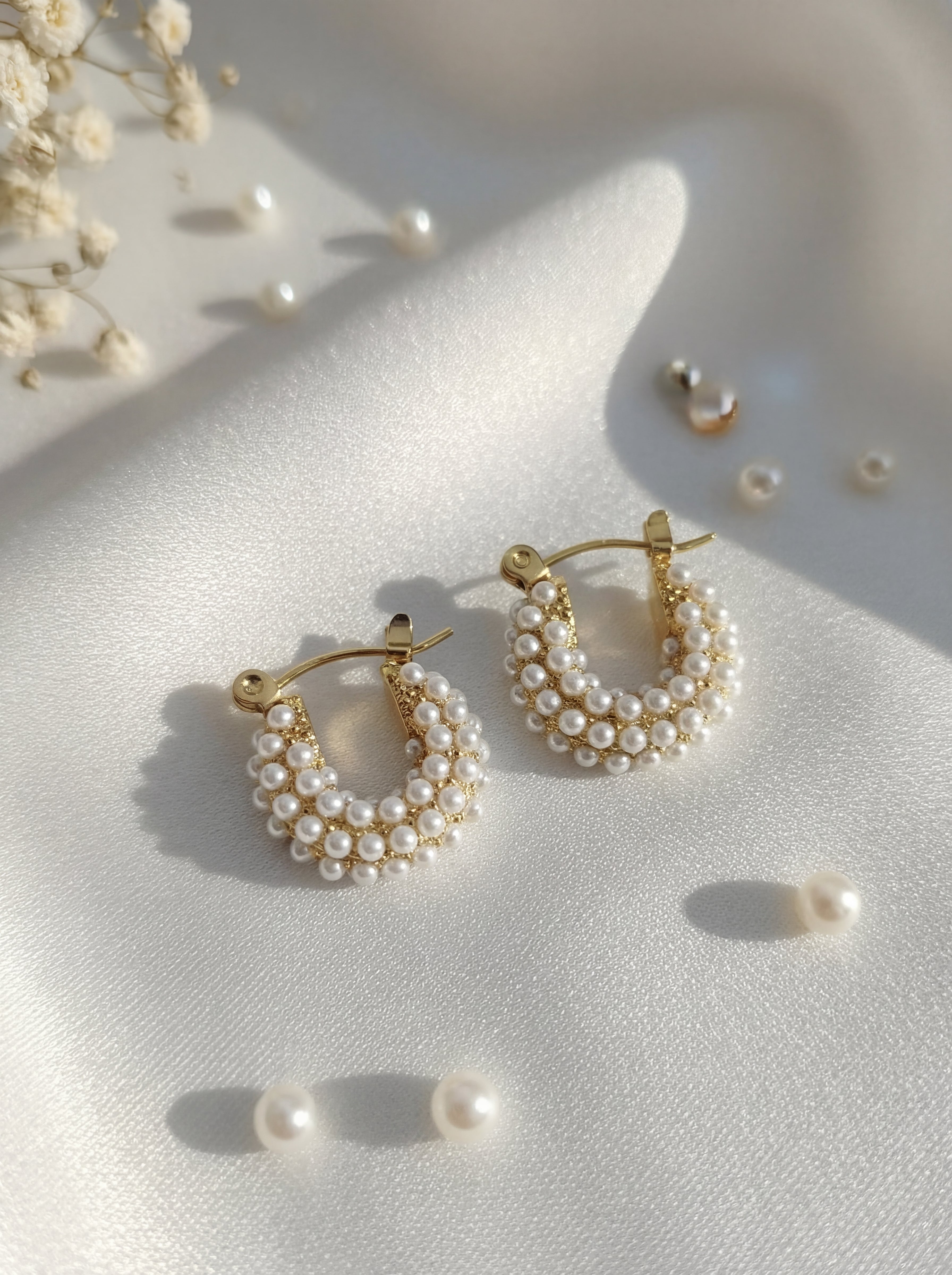 Pair of gold hoop earrings with pearl accents on a light surface.