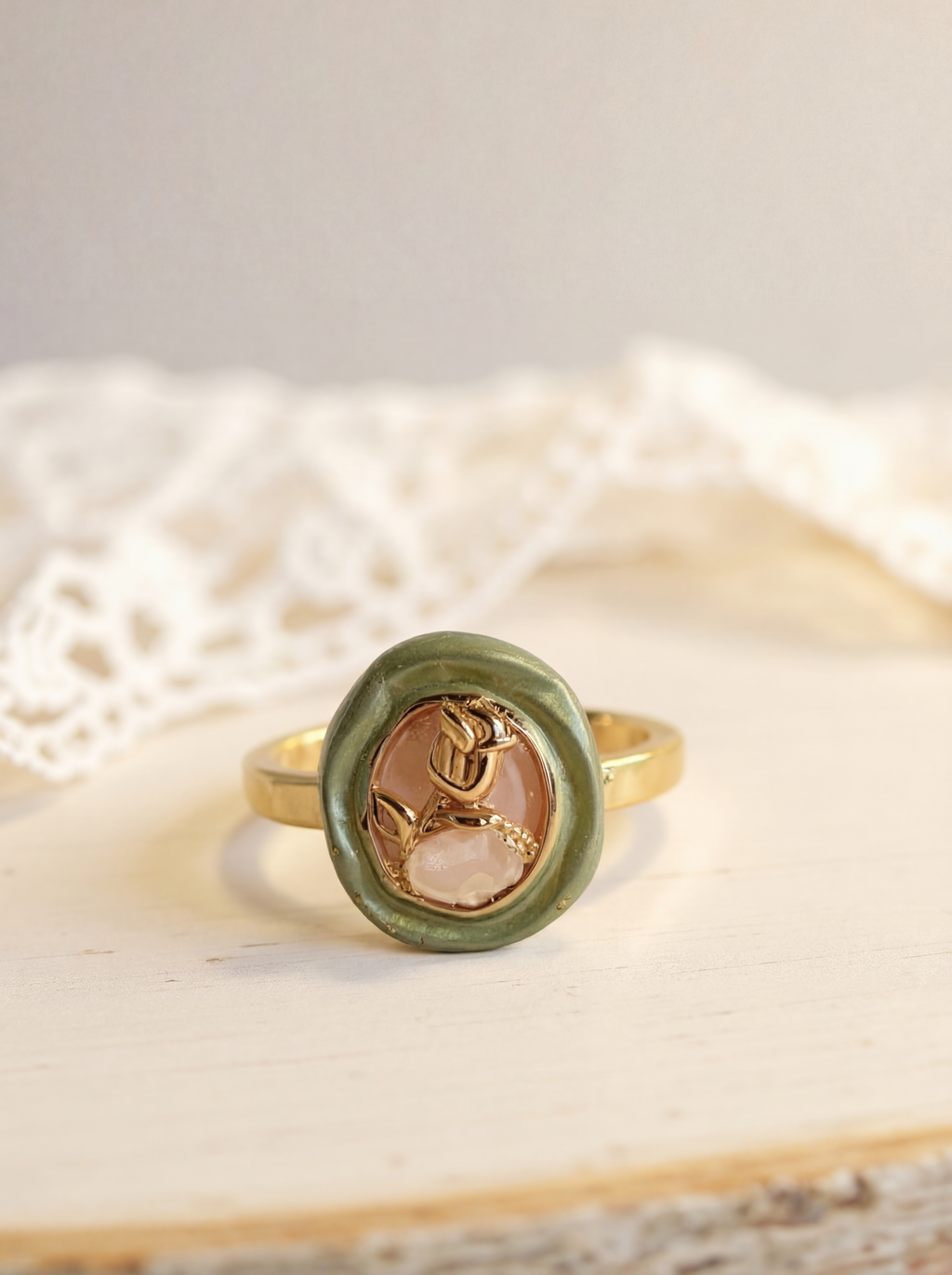 Gold ring with a green stone and rose design on a textured surface