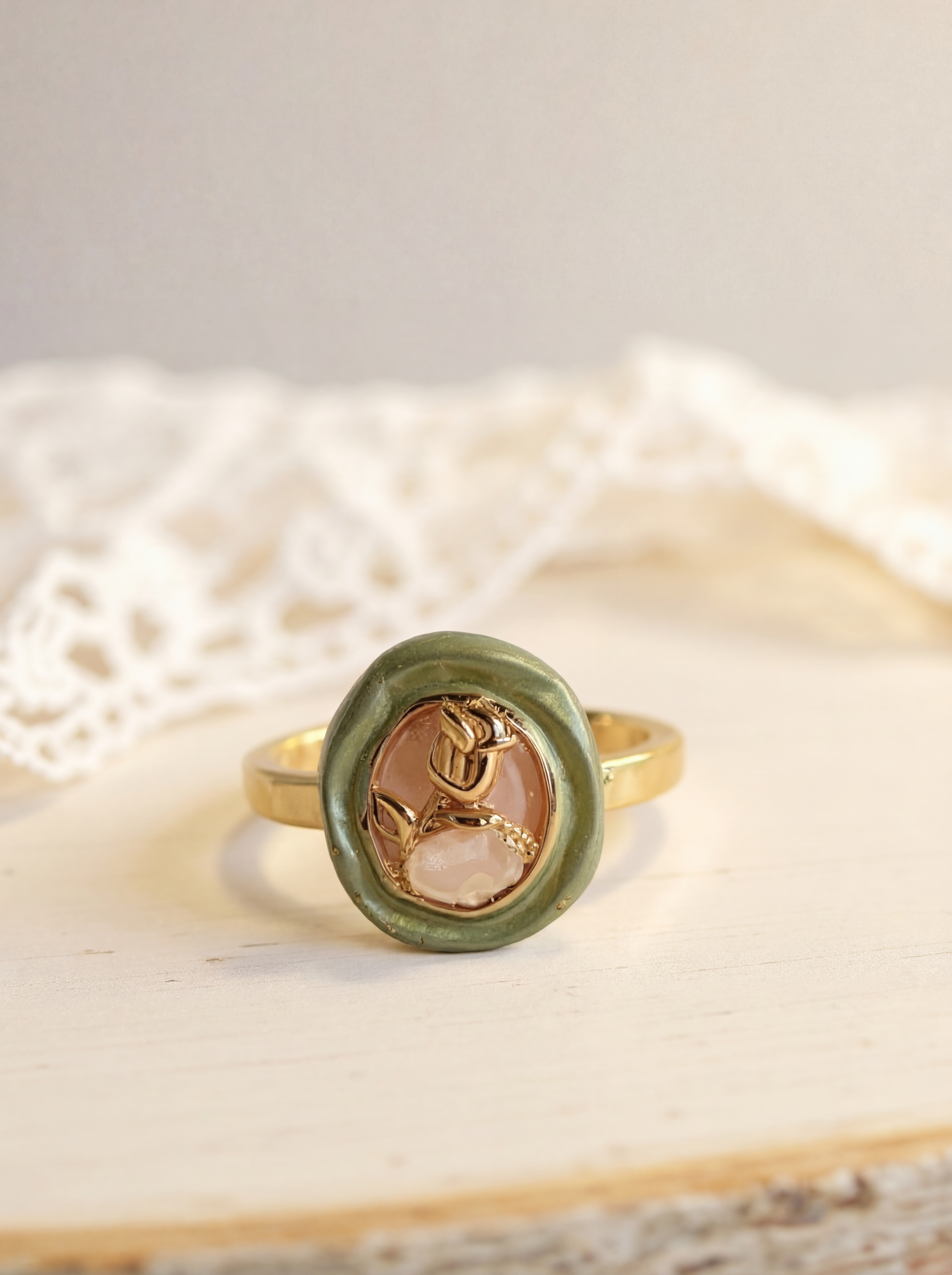 Gold ring with a green stone and rose design on a textured surface