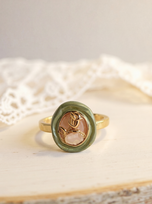 Gold ring with a green stone and rose design on a textured surface