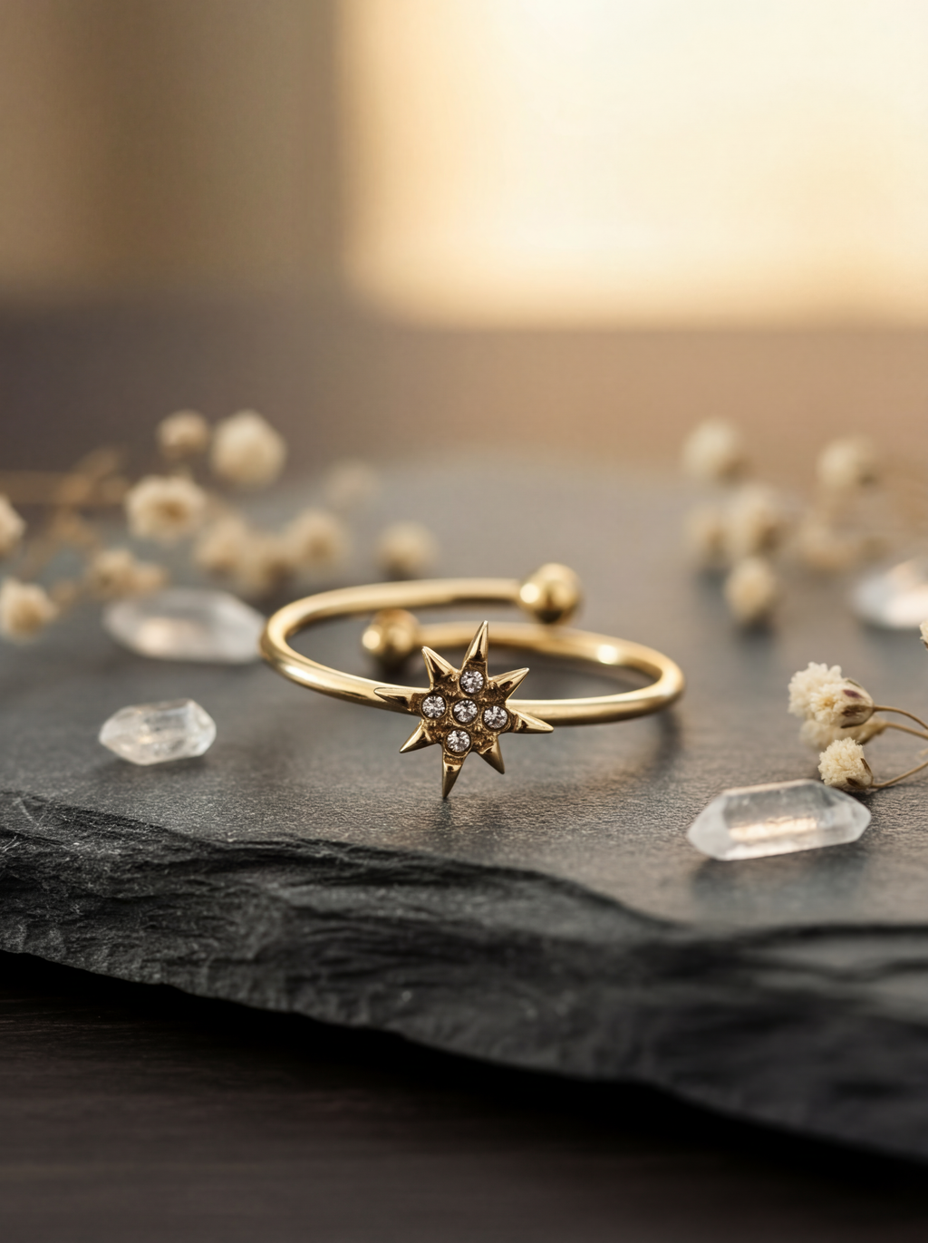 Gold star-shaped ring on a dark surface with small crystals and dried flowers.