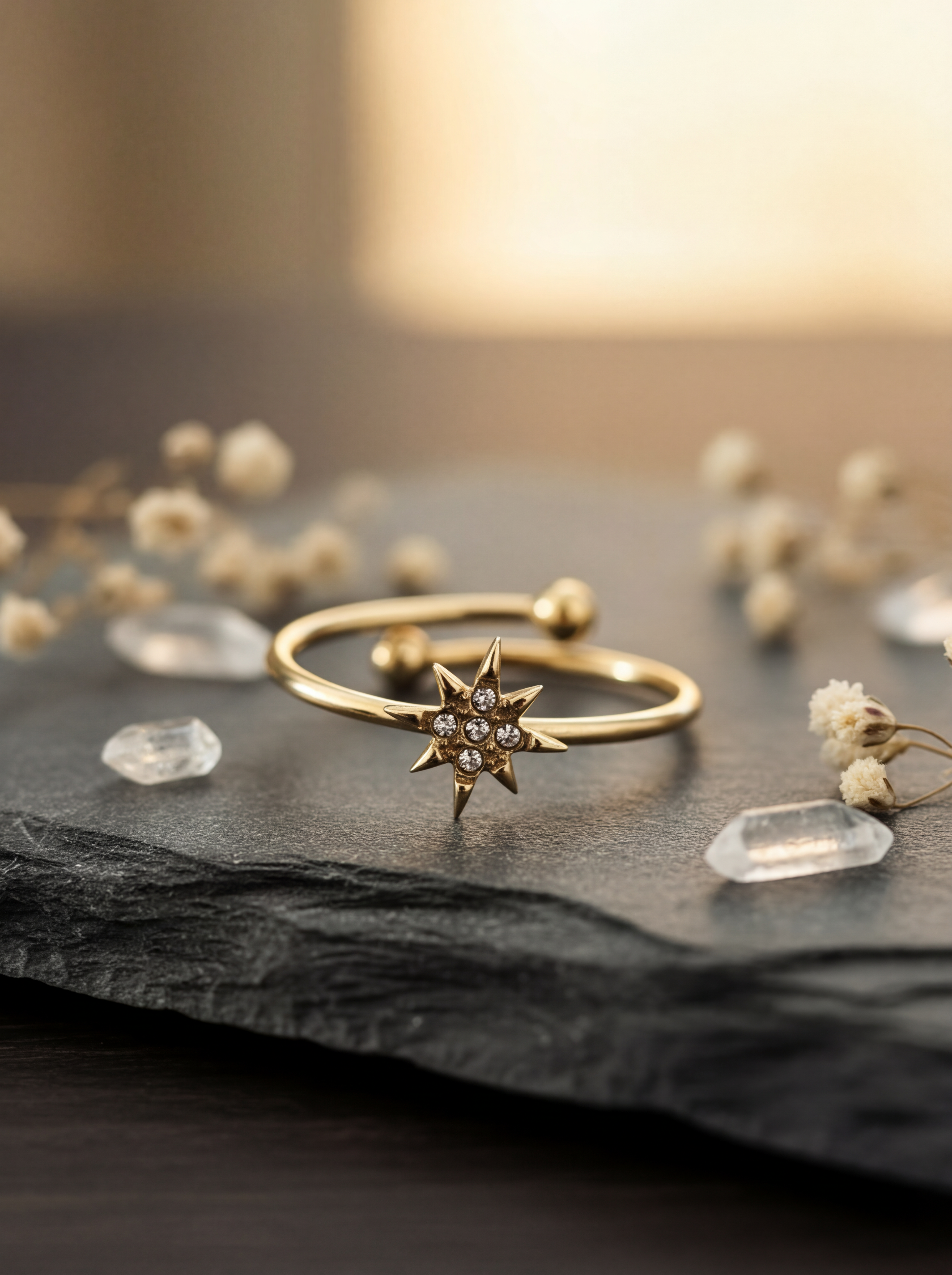 Gold star-shaped ring on a dark surface with small crystals and dried flowers.