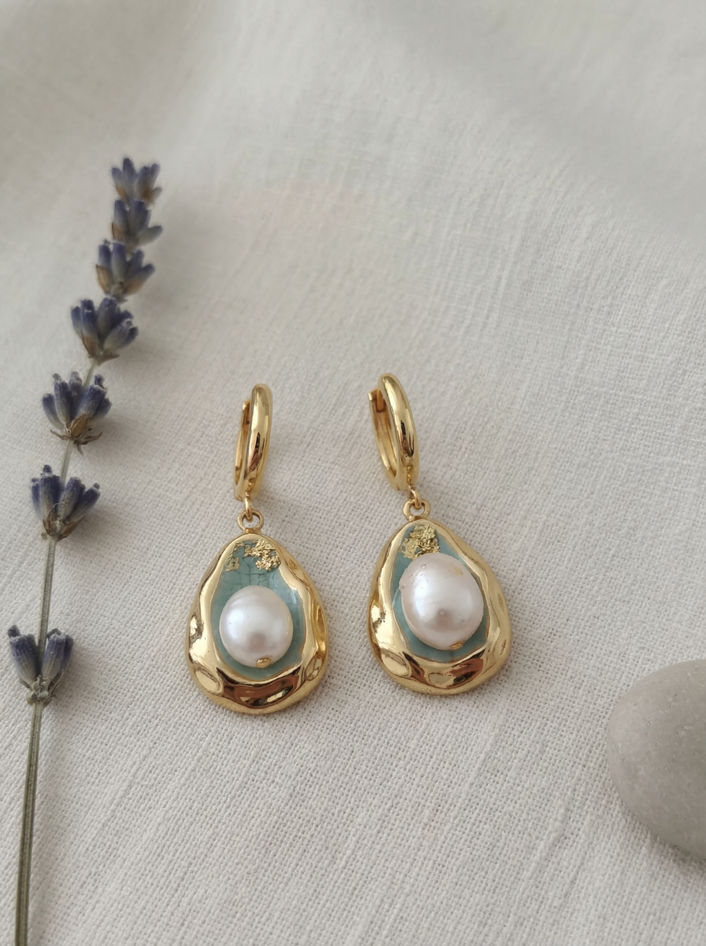 Gold earrings with pearls on a textured surface with lavender.