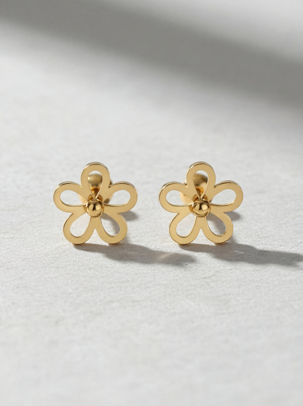 Gold flower-shaped earrings on a light gray background