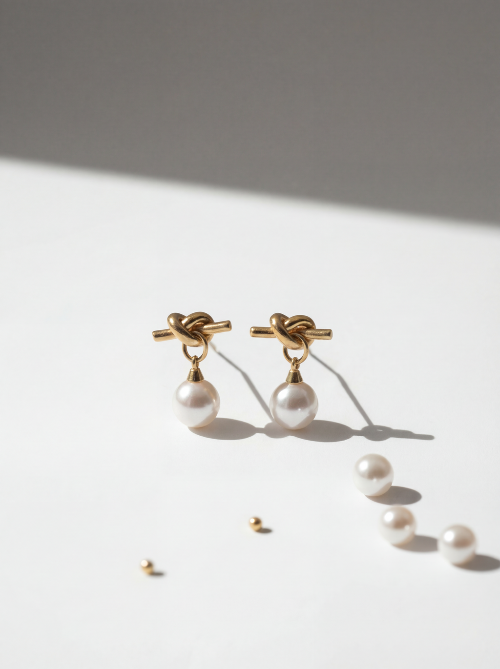 Pair of pearl earrings with gold knots on a light surface