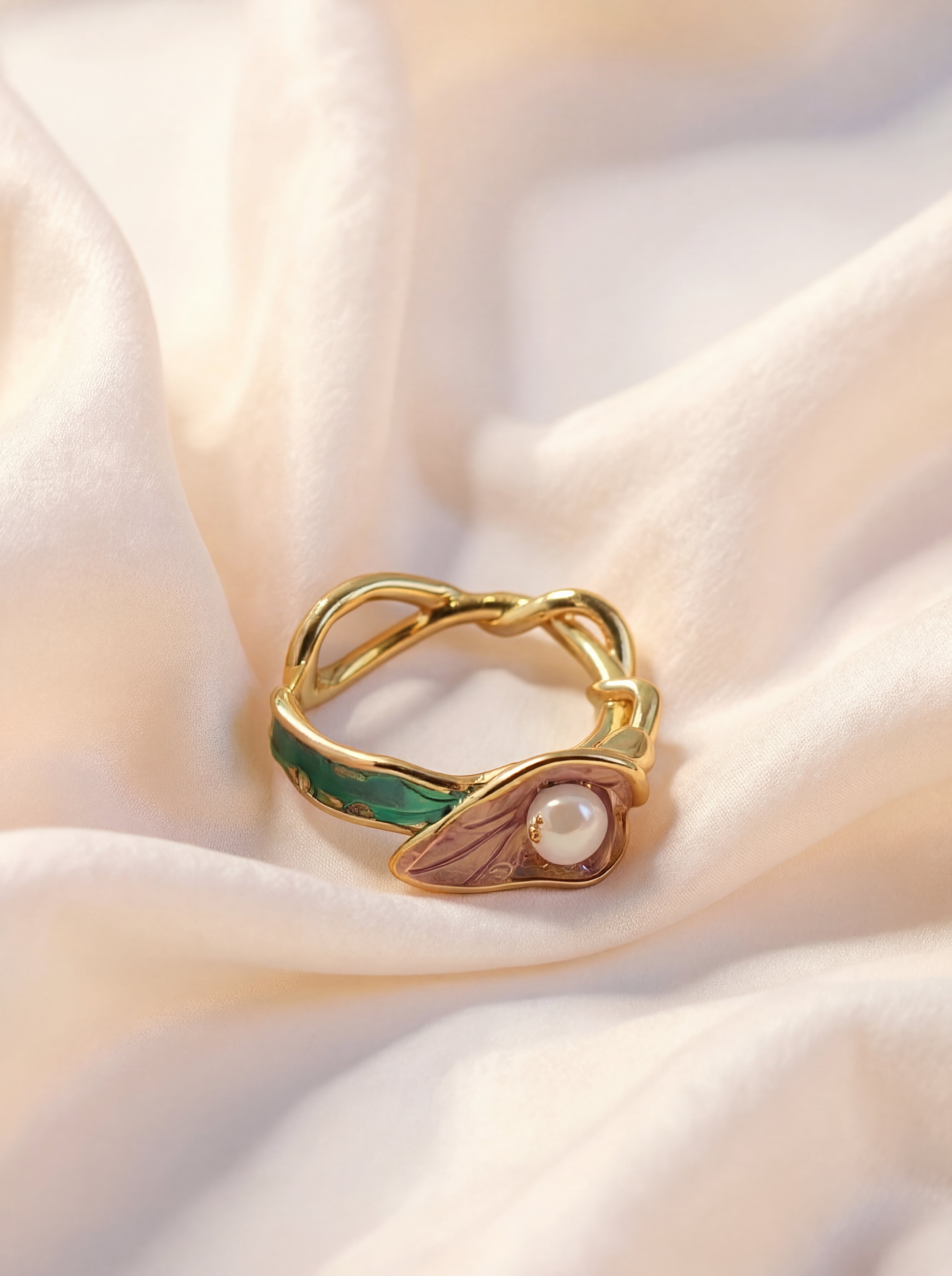 Gold ring with green and brown accents on a soft fabric background