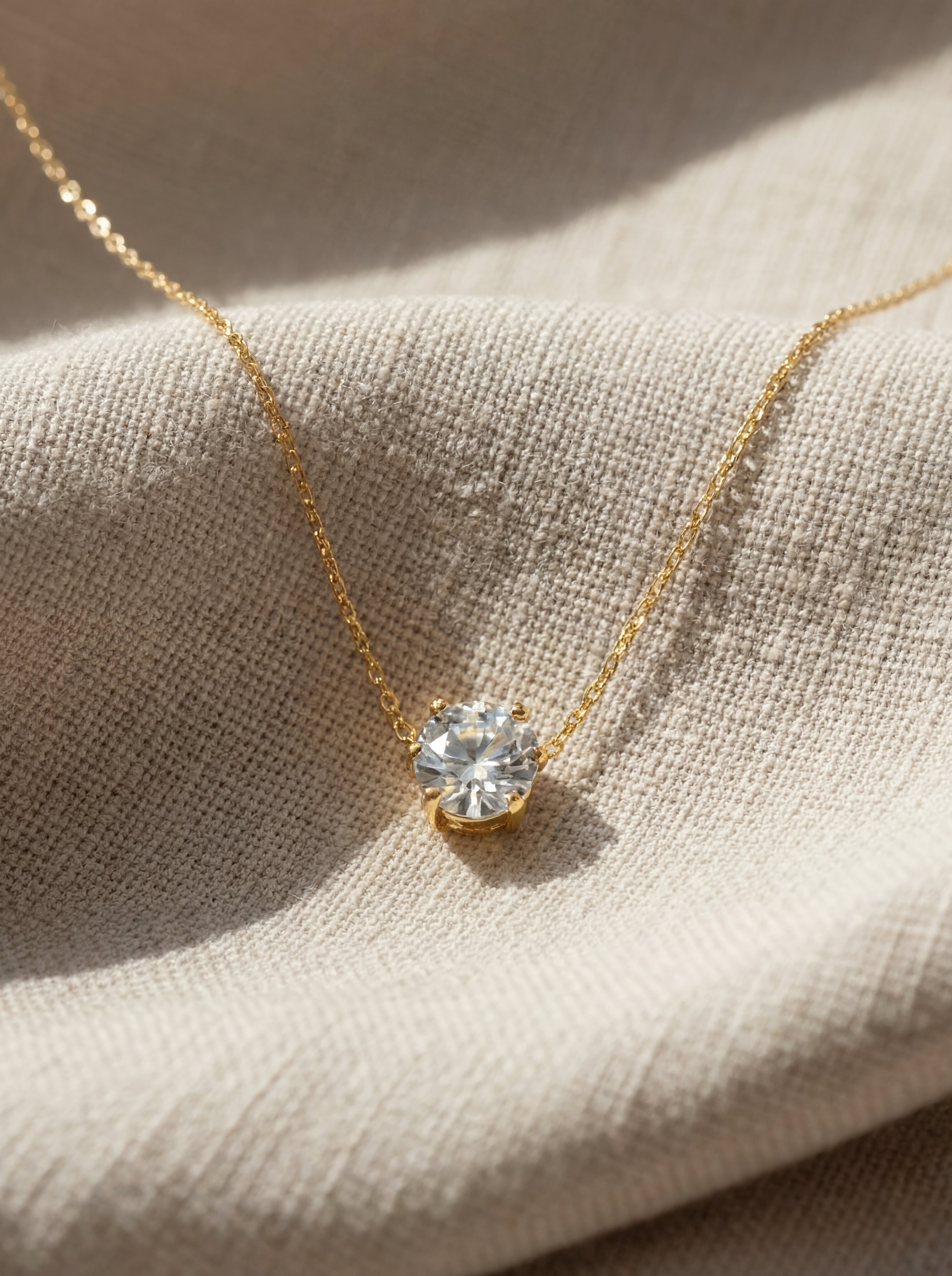 Gold necklace with a diamond pendant on a textured beige surface