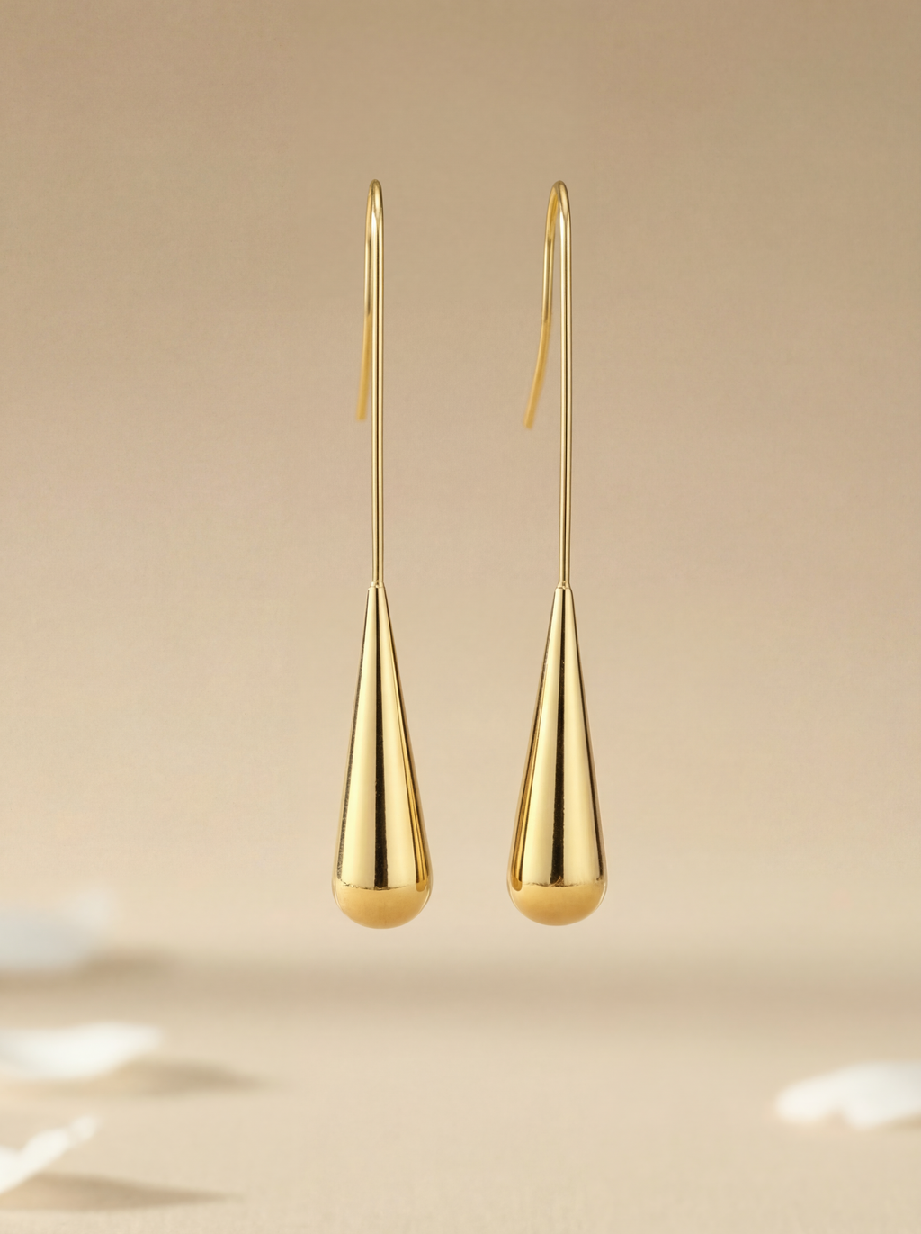 Gold teardrop earrings on a beige background