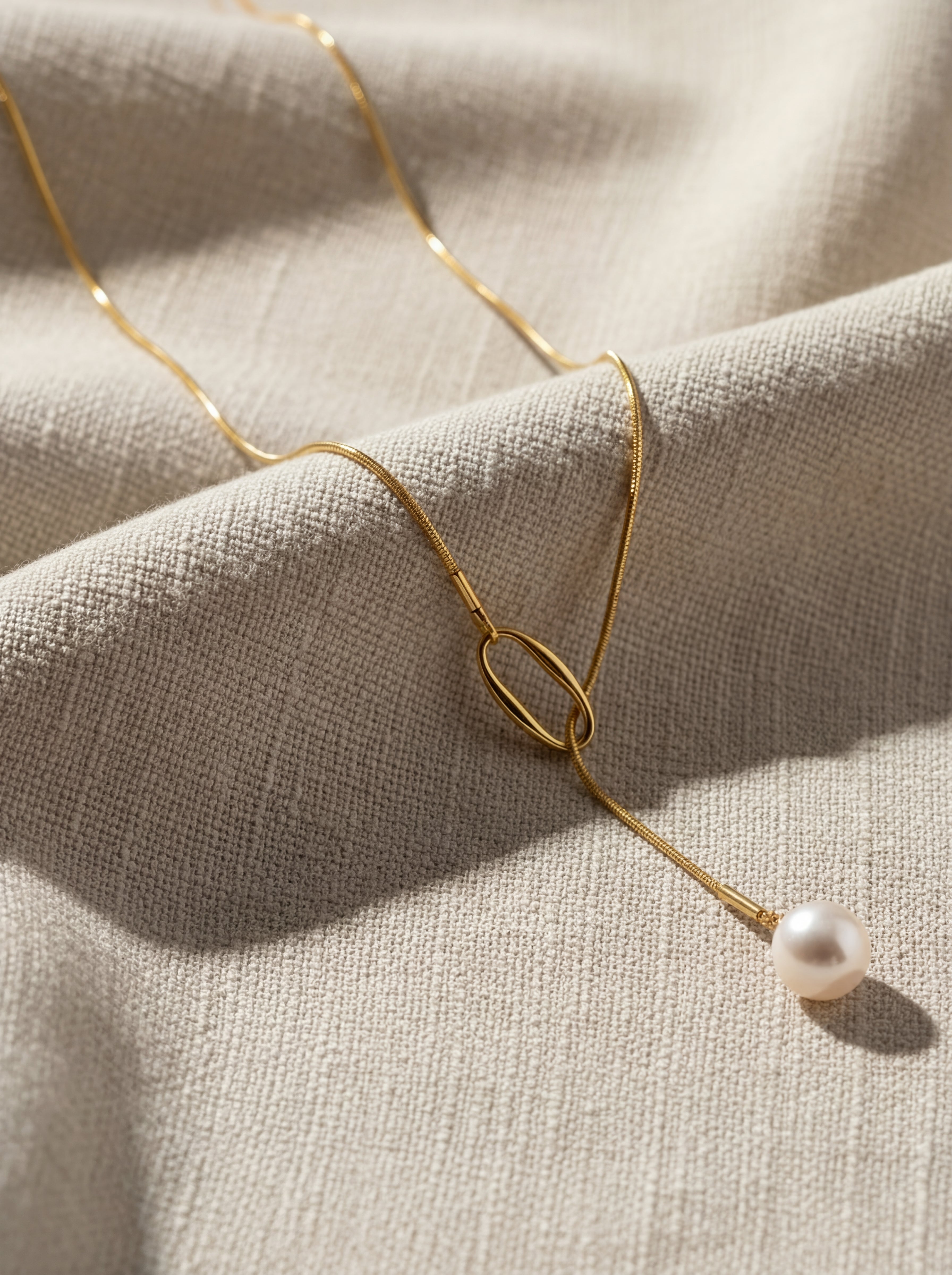 Gold necklace with a pearl pendant on a beige fabric background