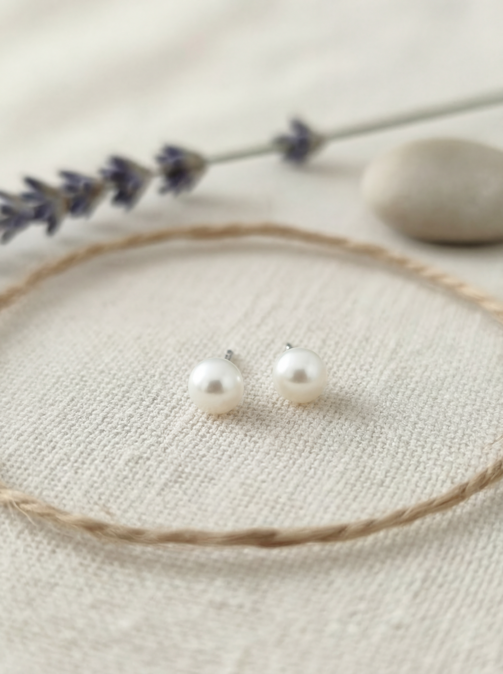 Pearl stud earrings on a beige surface with lavender and stones in the background