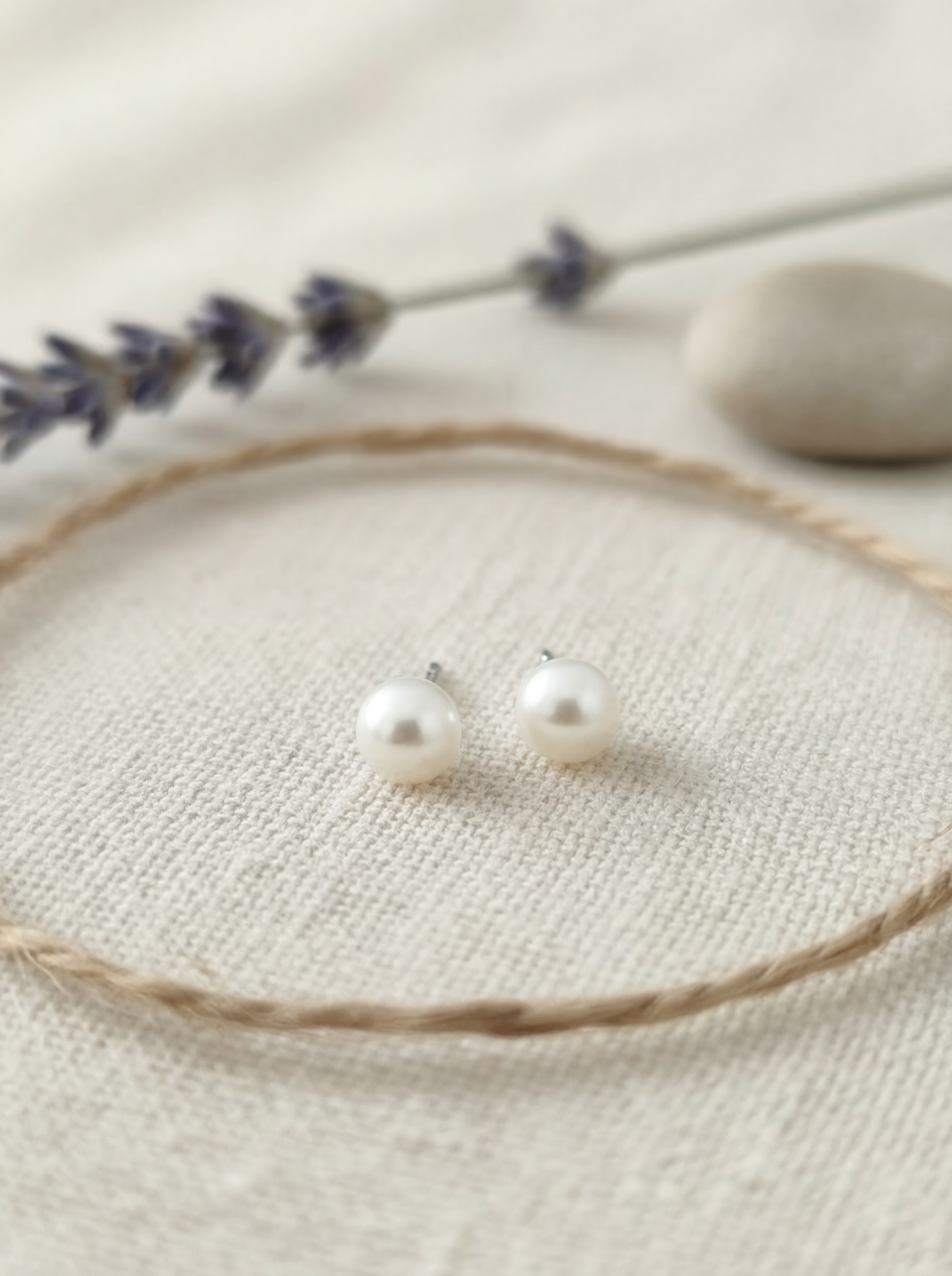 Pearl stud earrings on a beige surface with lavender and stones in the background