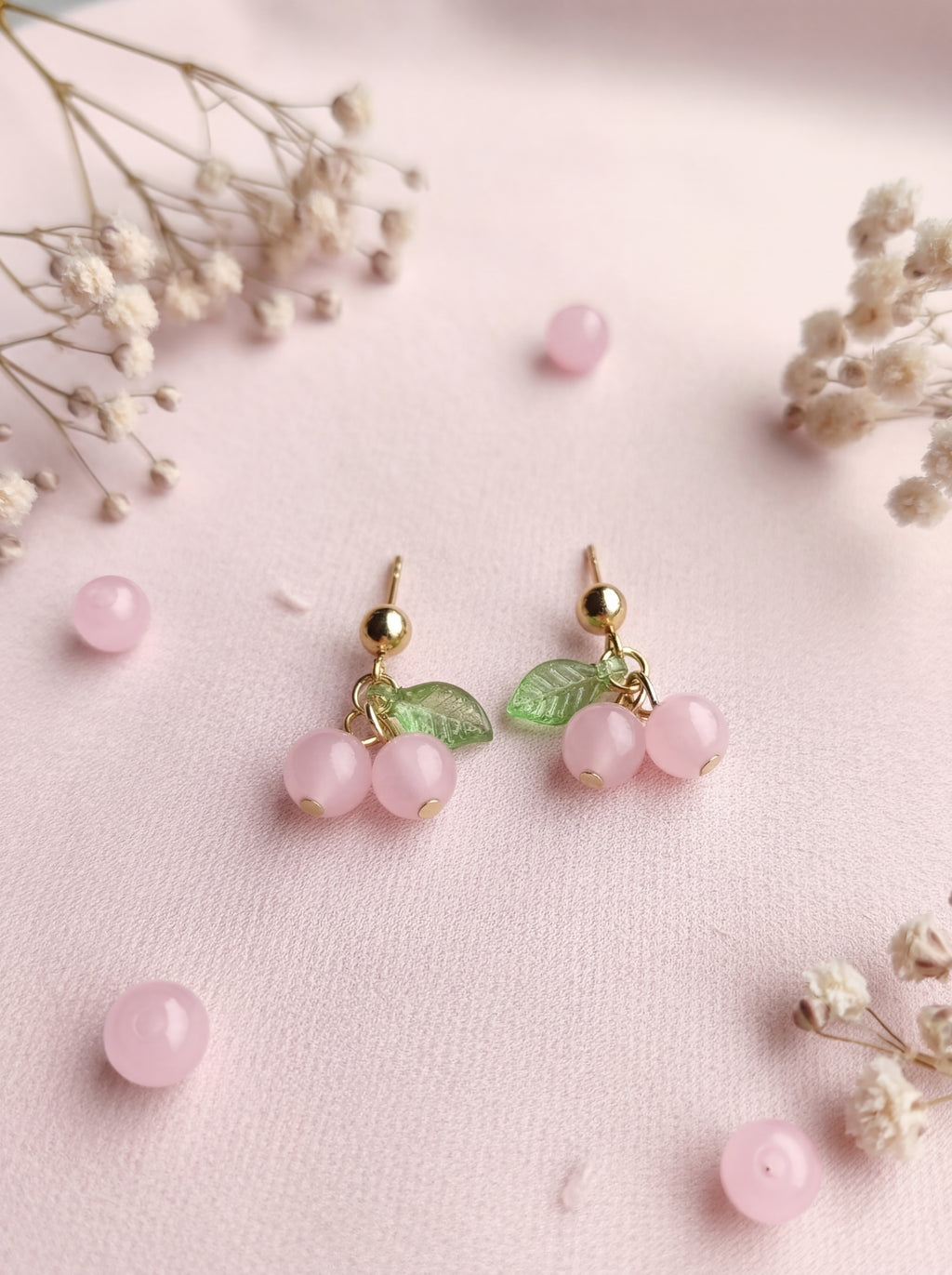 Pink berry earrings with gold accents on a pink background with small flowers.