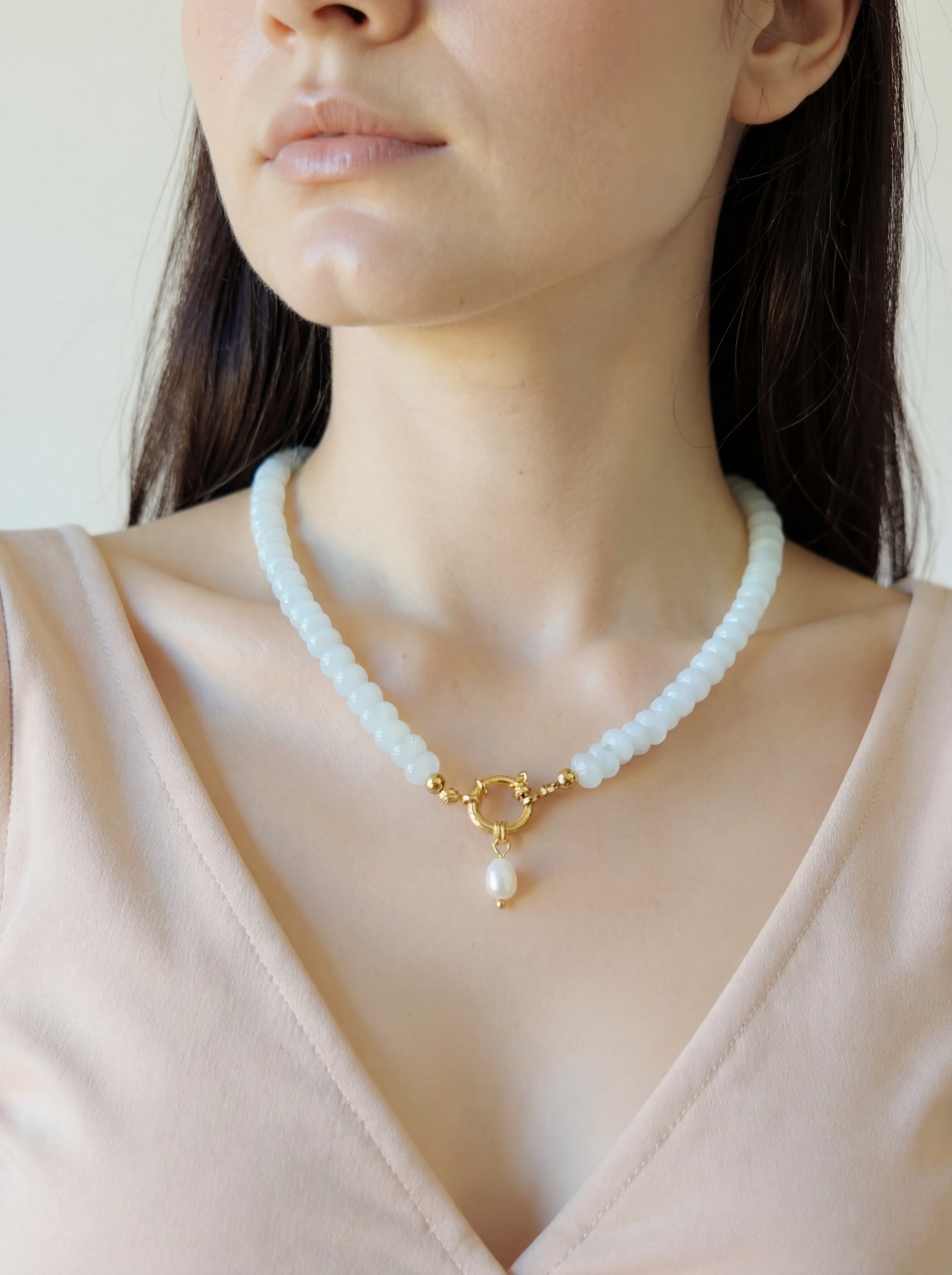Woman wearing a delicate necklace with a pearl pendant against a neutral background