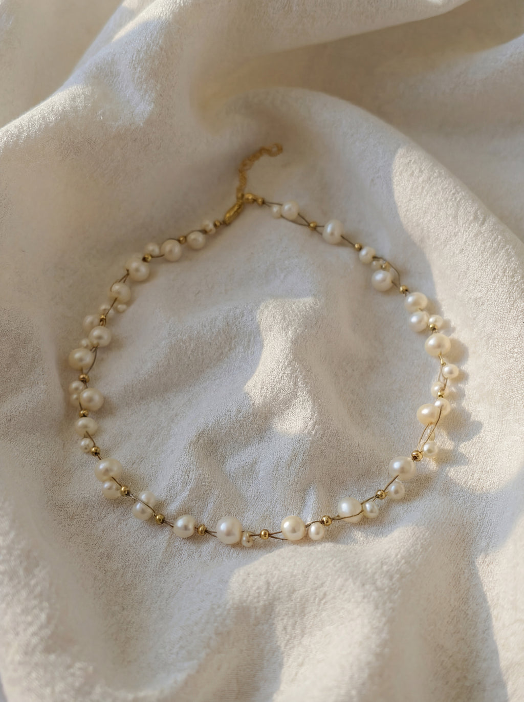 Pearl necklace with gold chain on a textured white surface