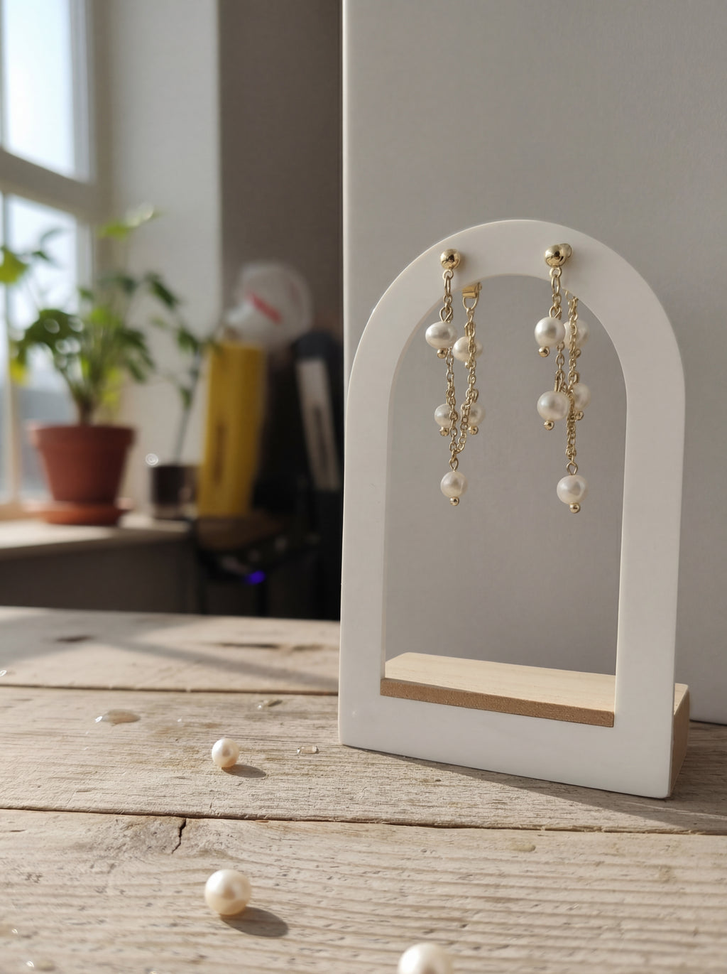 Pearl earrings on a white stand with scattered pearls on a wooden surface.