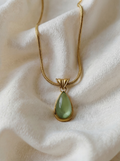 Gold necklace with a green teardrop pendant on a white fabric background