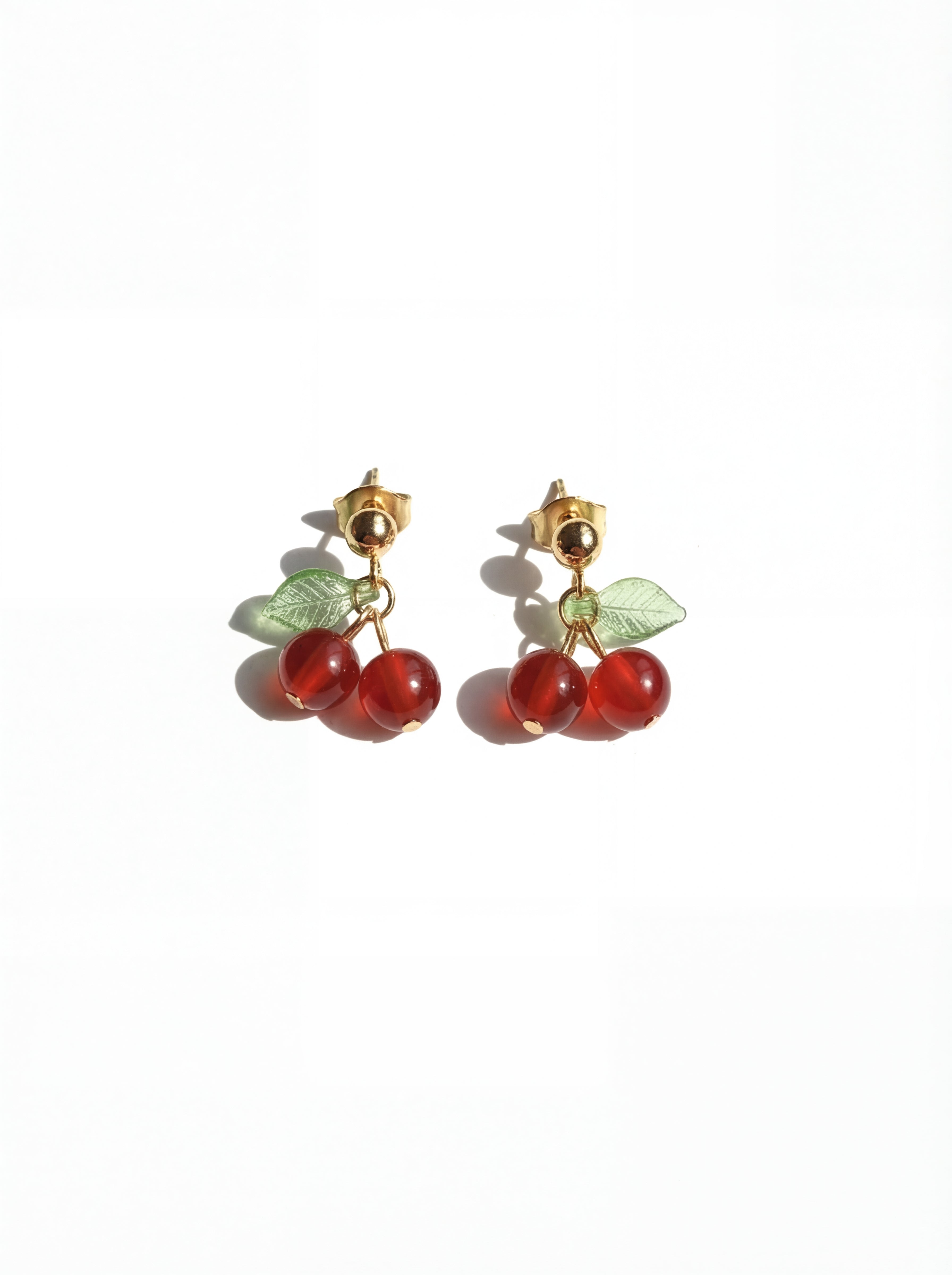 Cherry-themed earrings with red stones and gold accents on a white background