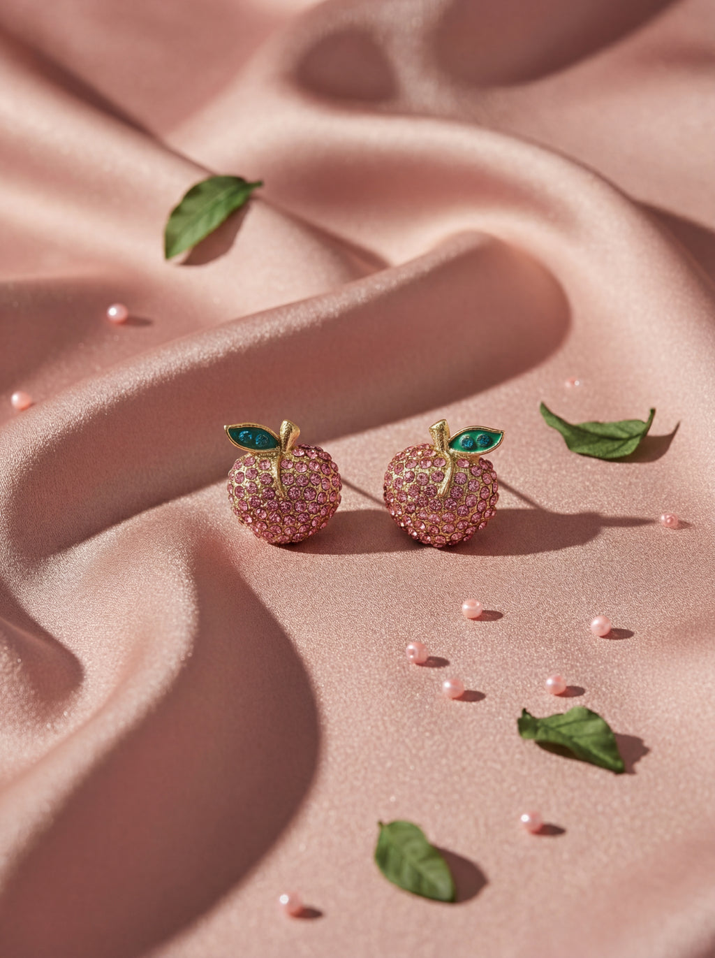 Pink apple-shaped earrings with green leaves on a pink fabric background
